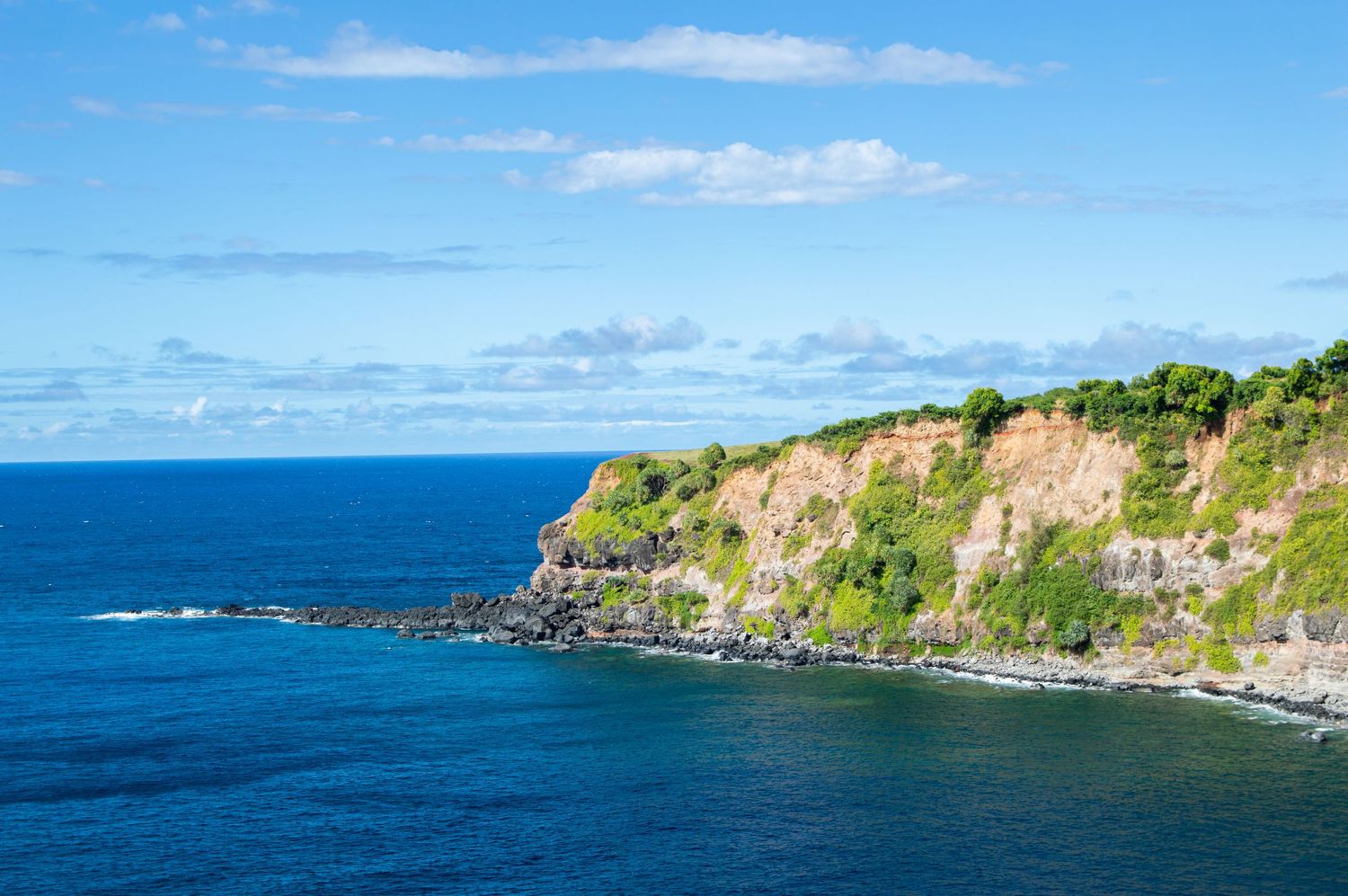 Scenic coastal cliffs rising above deep blue ocean waters under bright blue sky.