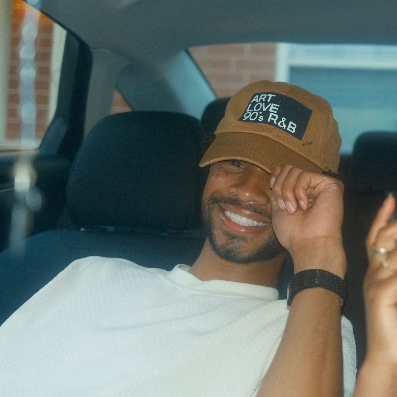 Person wearing a baseball cap smiling while sitting in a vehicle interior.