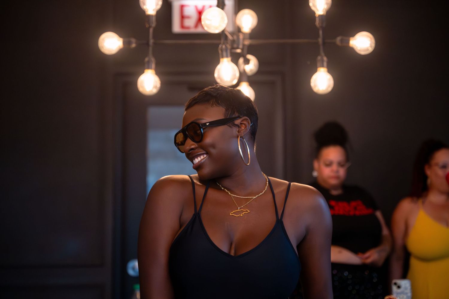 Person wearing sunglasses dancing under pendant lights at nighttime event.