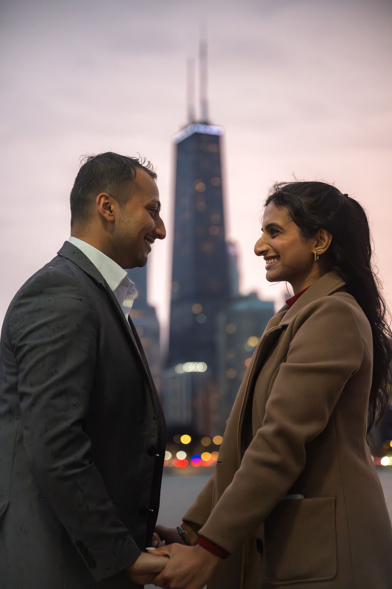 Couple sharing romantic moment with Chicago's Hancock Tower in background at dusk.