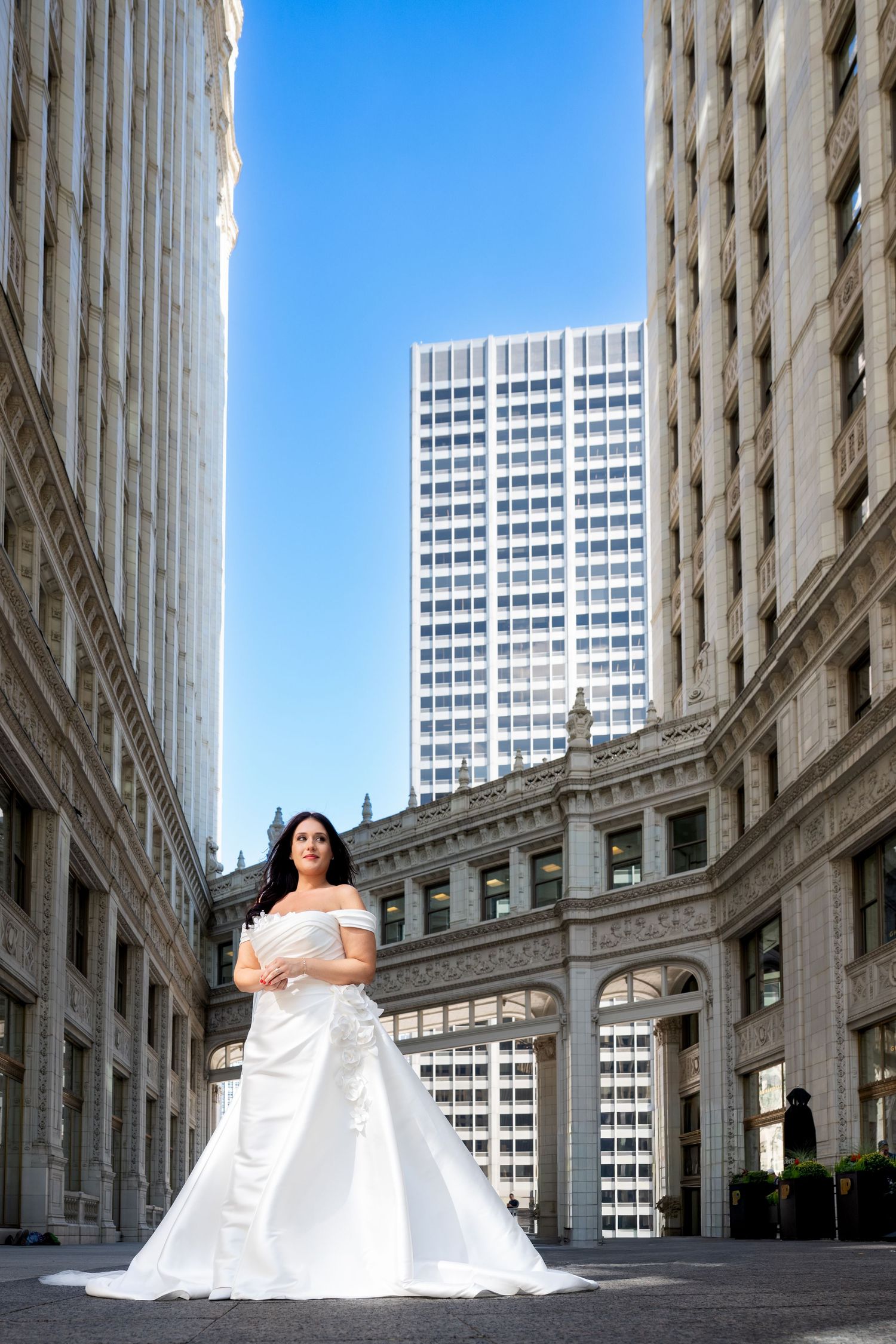 A white wedding dress contrasts against classic architecture and modern skyscrapers in an urban setting.