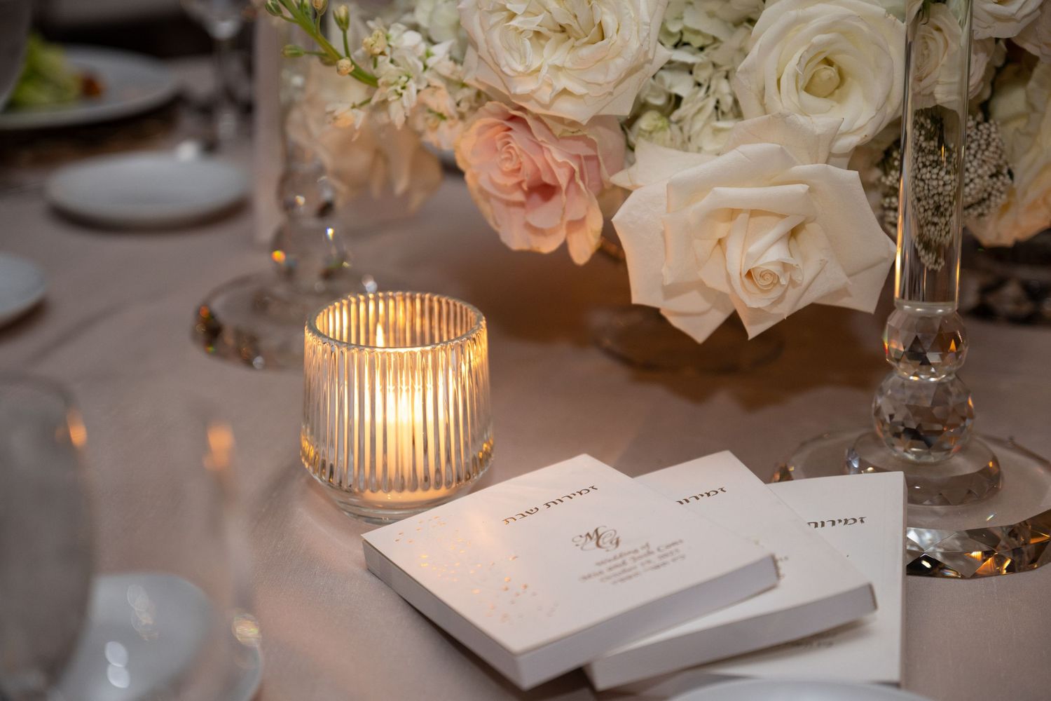 Elegant wedding reception table setting with white roses, glowing candles, and delicate place cards.