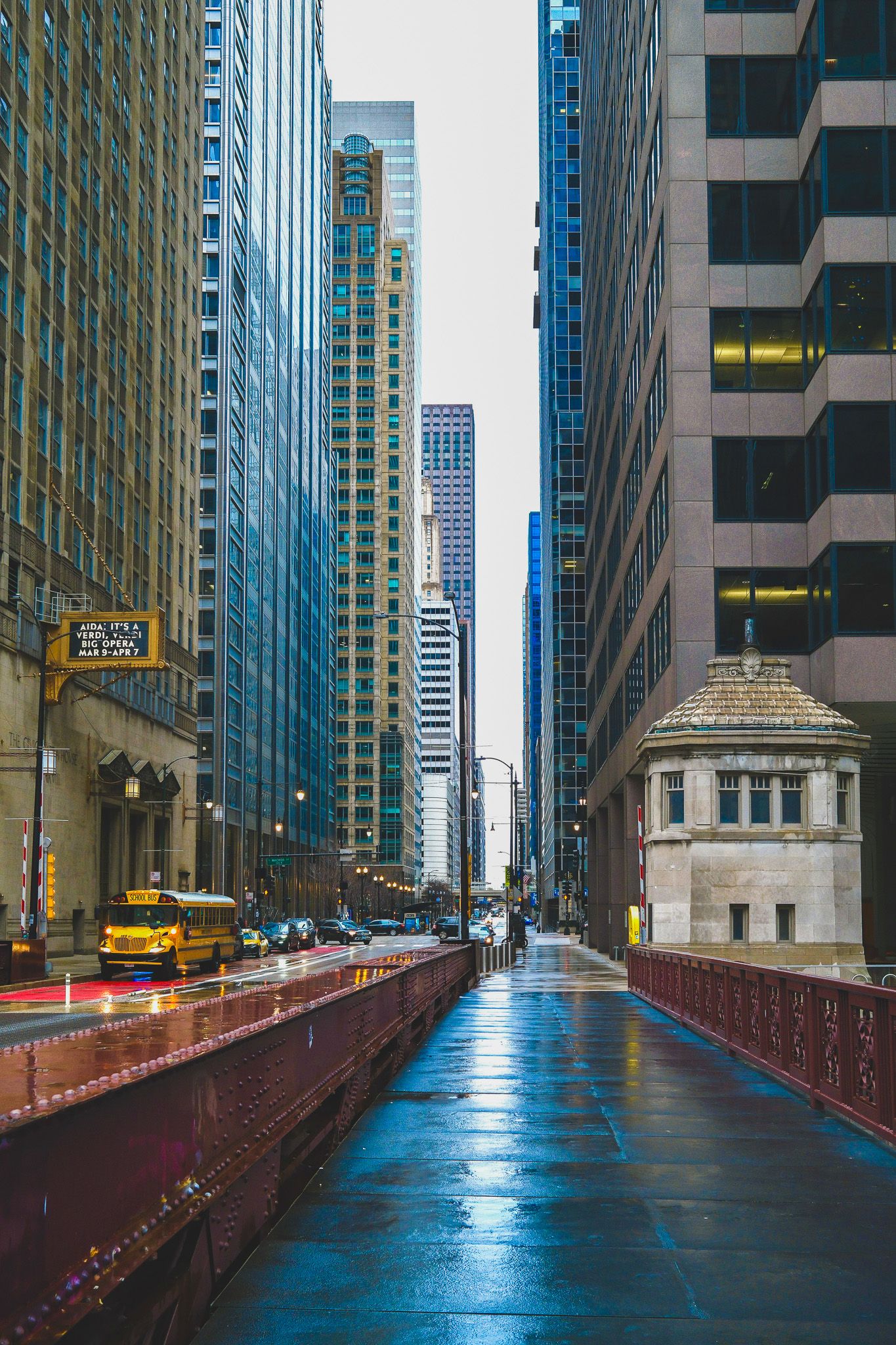 Wet city street between modern skyscrapers with yellow taxi and reflective surfaces in downtown Chicago.