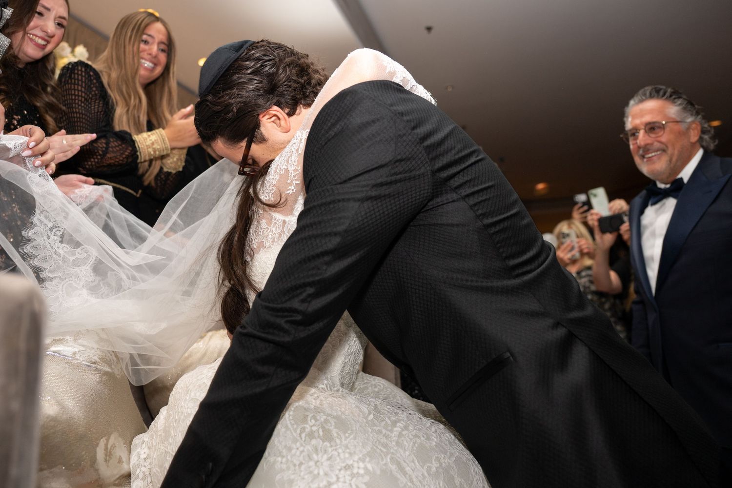 A joyful wedding celebration moment with the groom reaching under the bride's dress for the garter during the reception.