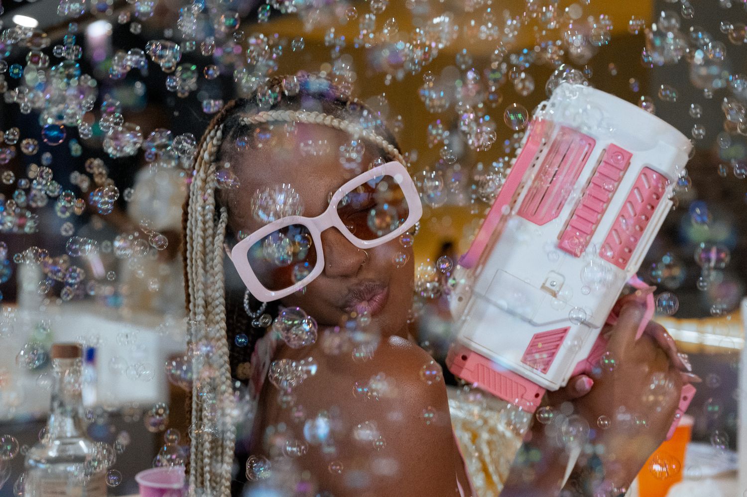 Playful portrait with bubbles and pink drink against warm background.