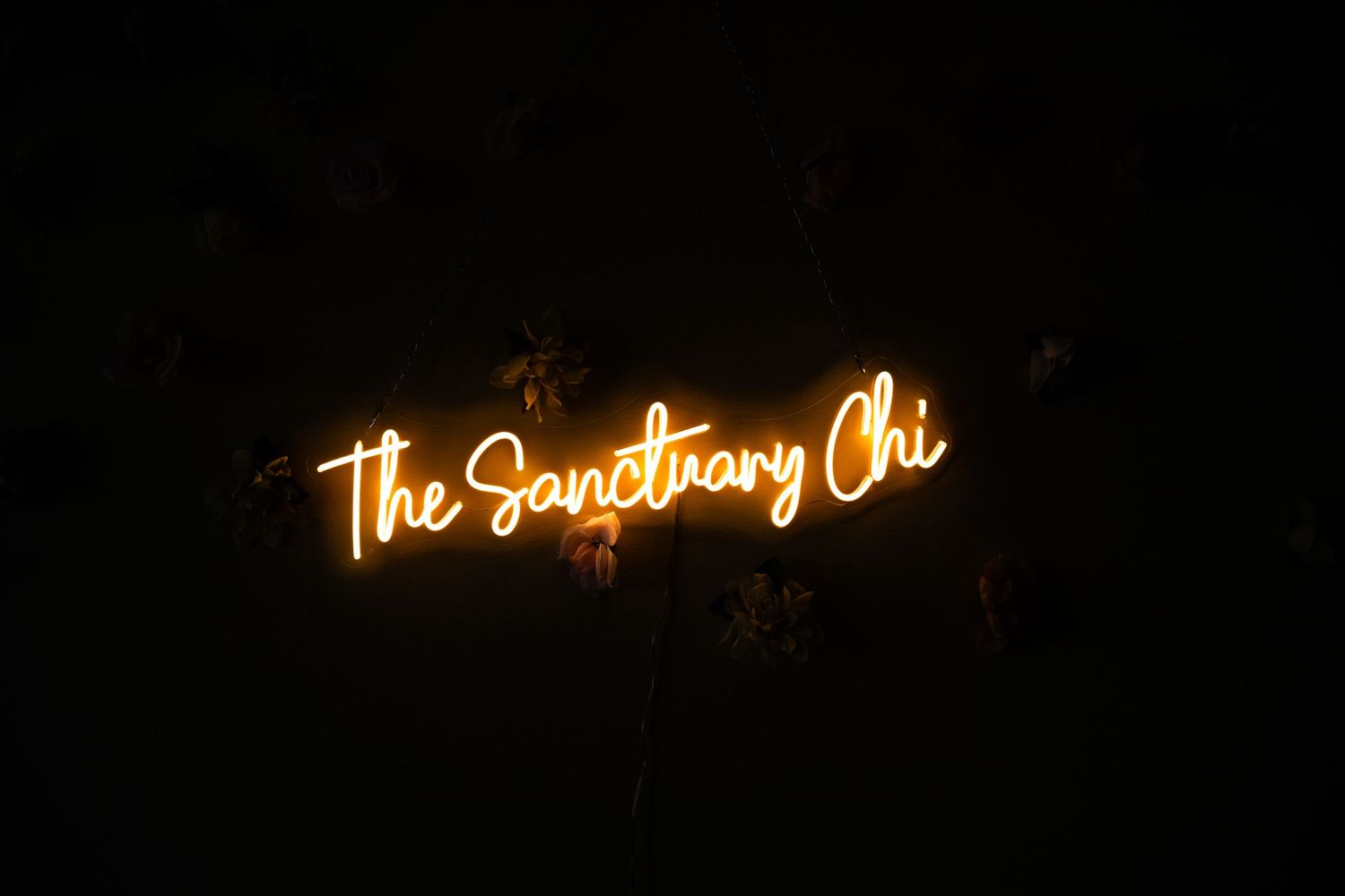 Neon sign reading 'The Sanctuary Chi' glowing in darkness.