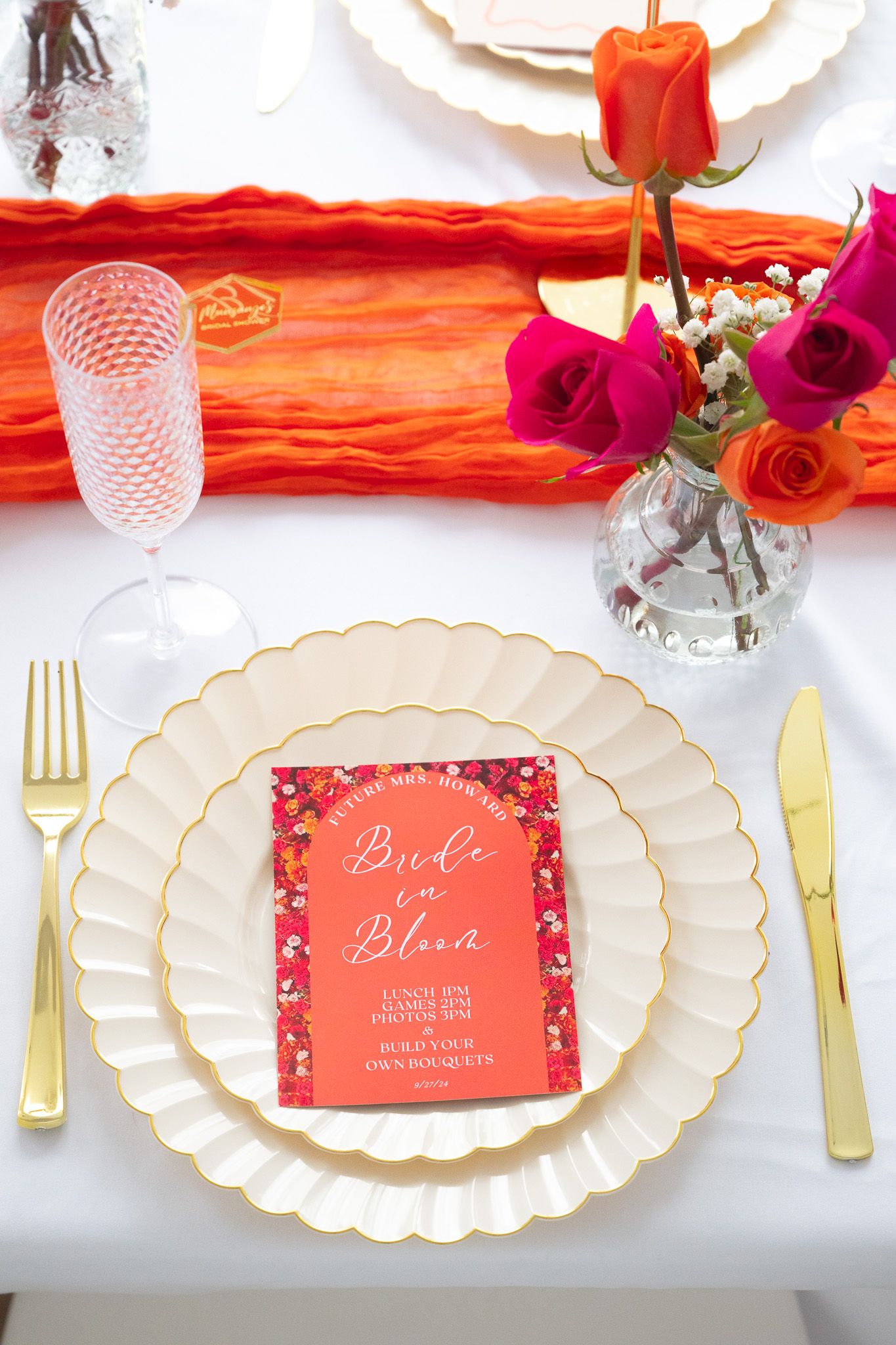 Elegant table setting with scalloped plates, coral menu card, and fresh roses in a glass vase.