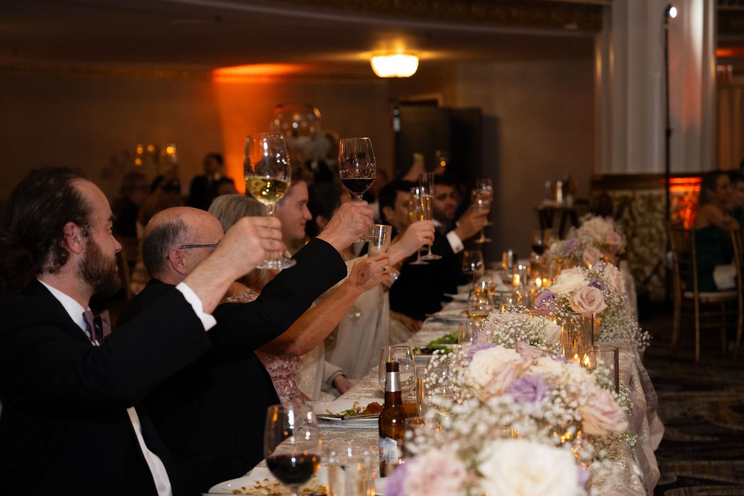 Wedding reception guests seated at elegant tables with glowing candles and floral centerpieces in a dimly lit venue.