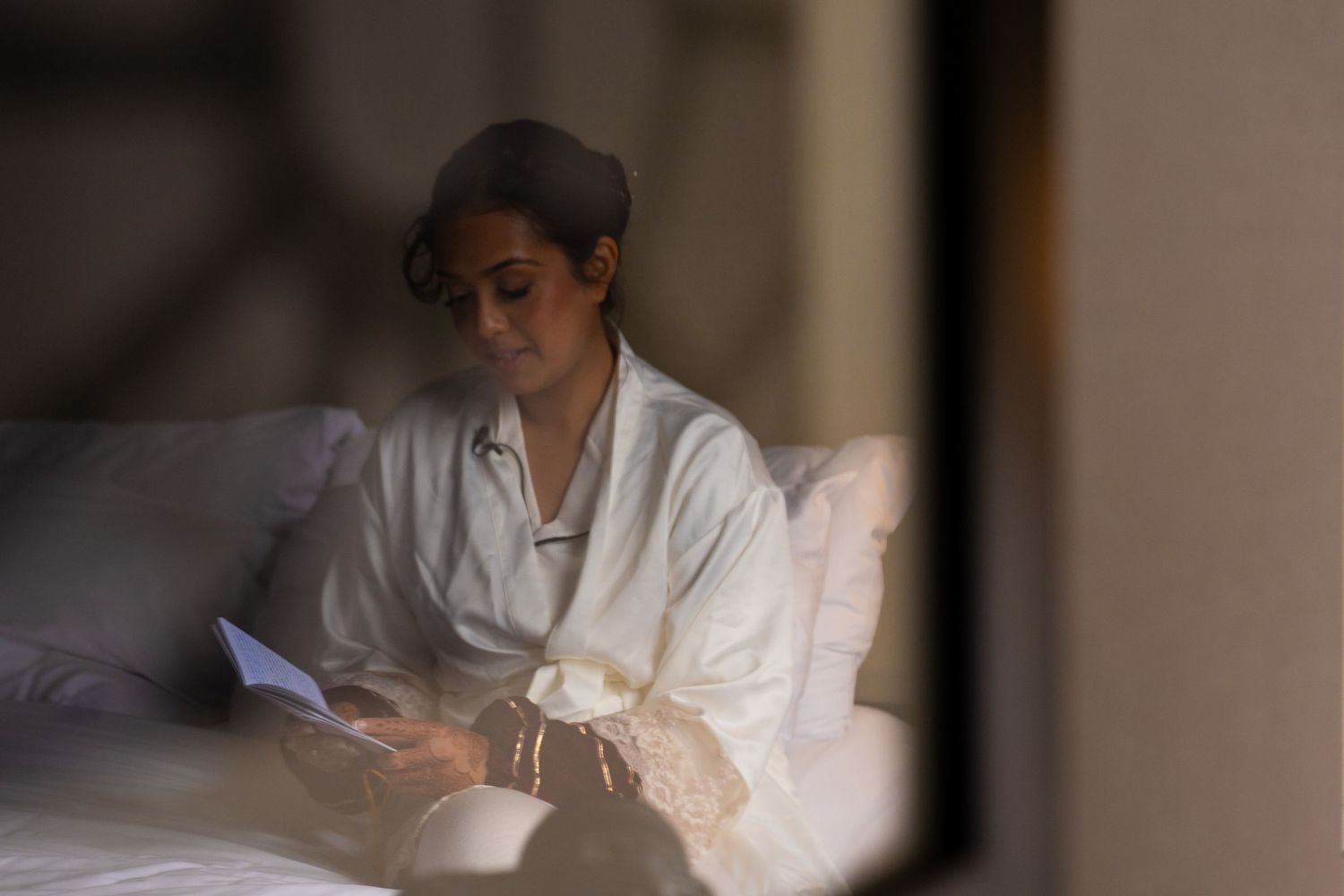 A person in white medical attire examines documents at a desk in a dimly lit room.
