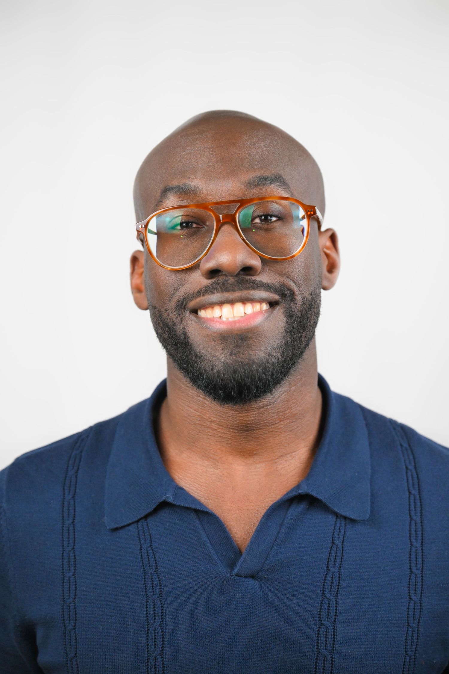 Professional headshots of person in navy polo shirt wearing glasses with warm smile.