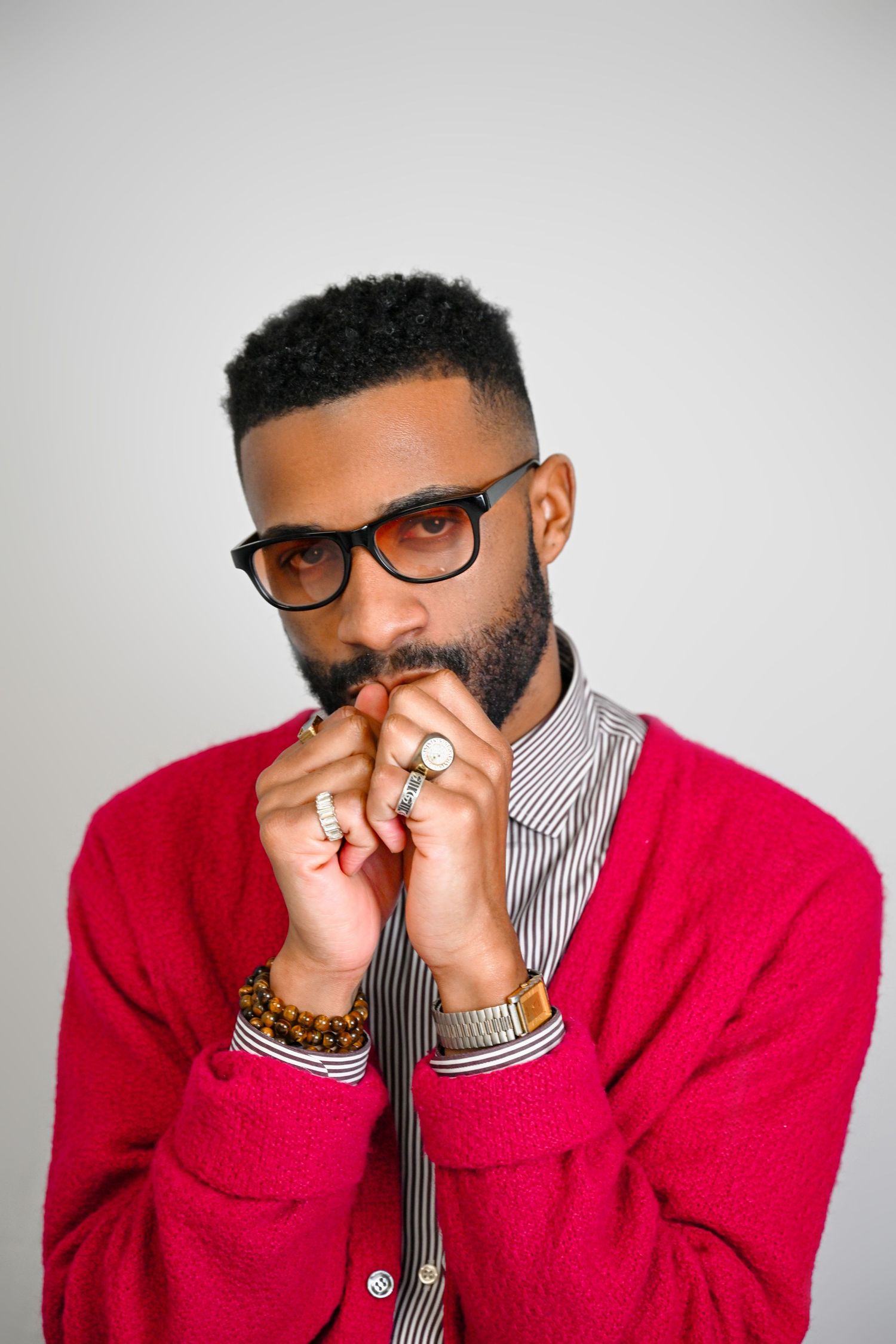 Person in red sweater and striped shirt wearing glasses poses expressively against white background in photo series.