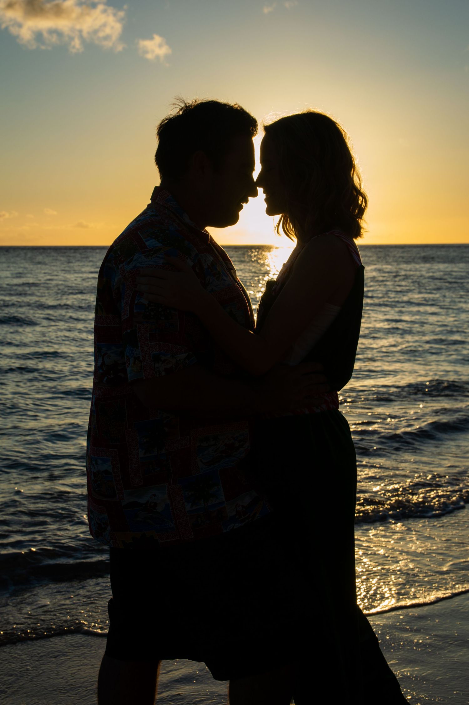 Silhouette of couple embracing at sunset on beach with ocean in background.