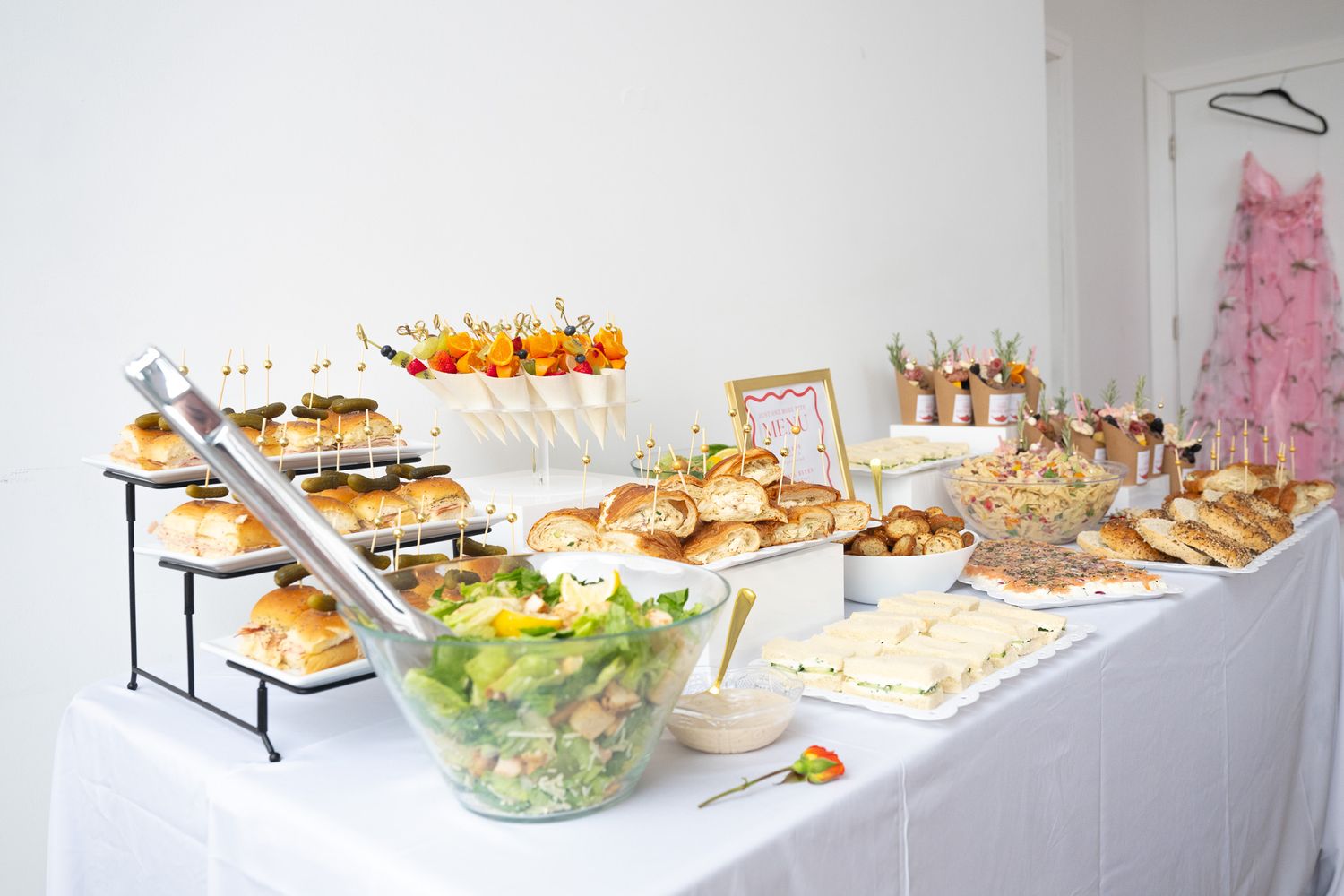 Elegant buffet display with tiered appetizers, sandwiches and salads on a white tablecloth.