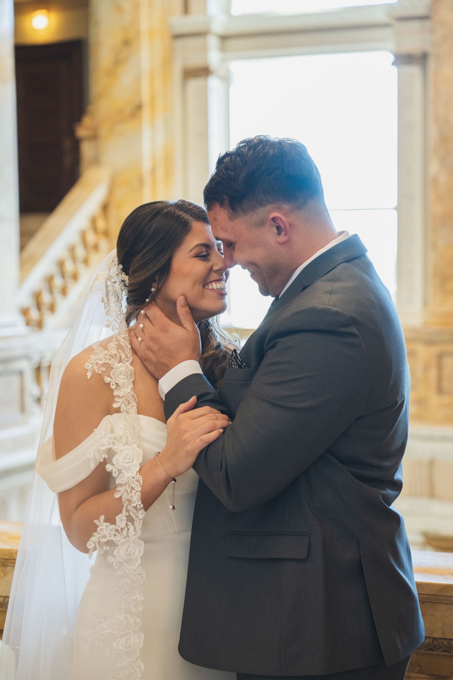 Intimate moment between newlyweds sharing tender embrace near bright window.