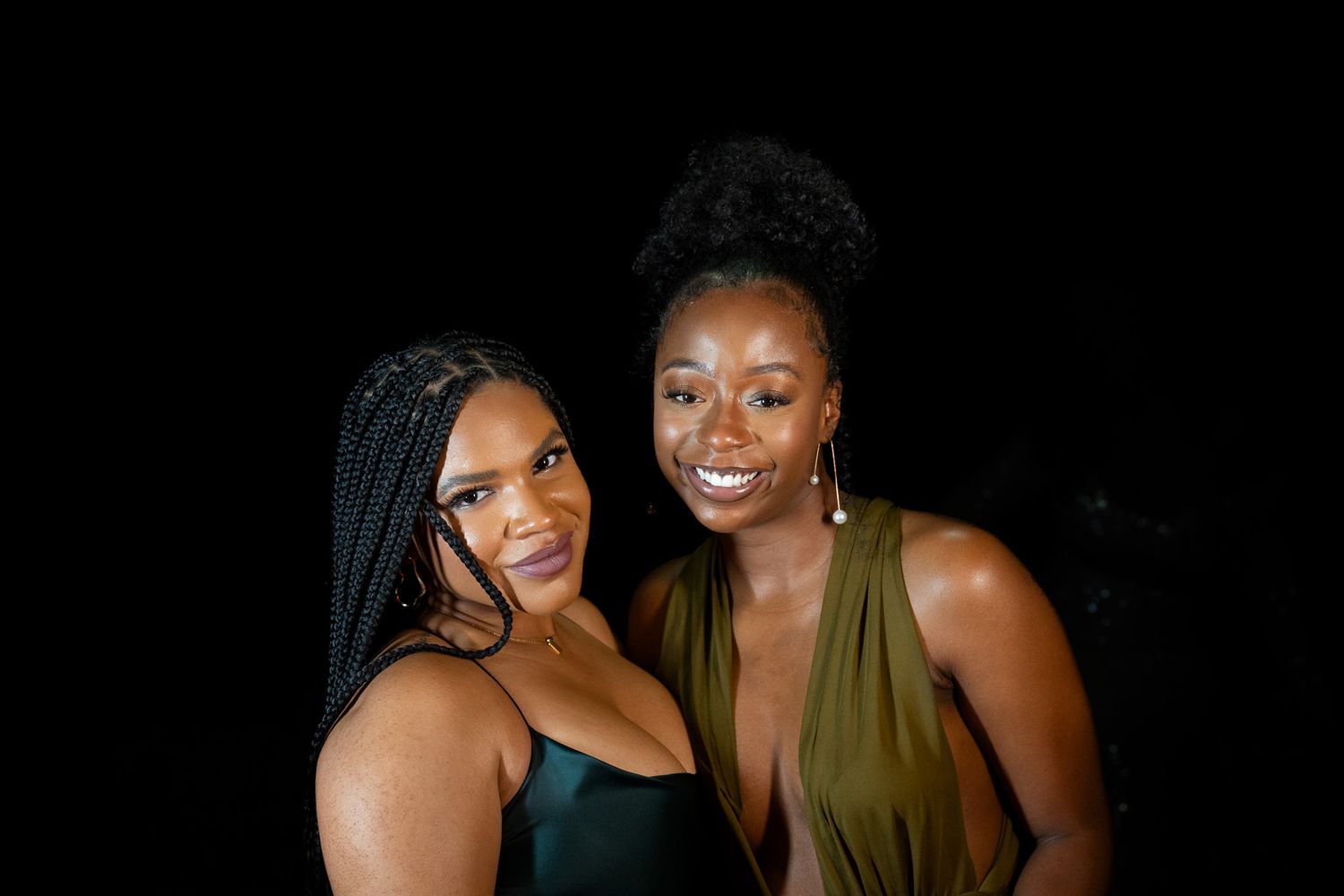 Two friends pose for portrait against black background.