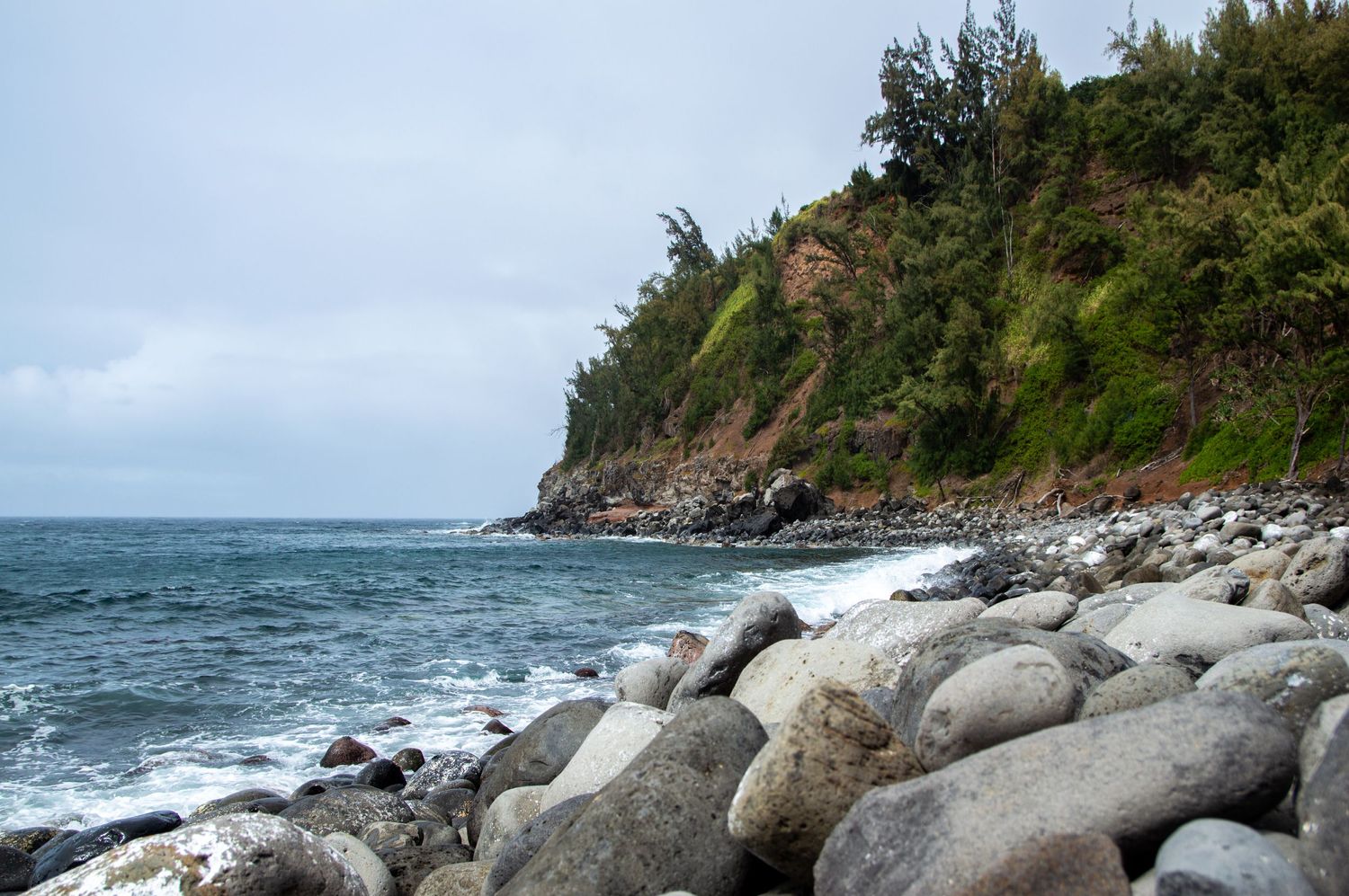 Rocky beach with large boulders against steep coastal cliffs and crashing waves.