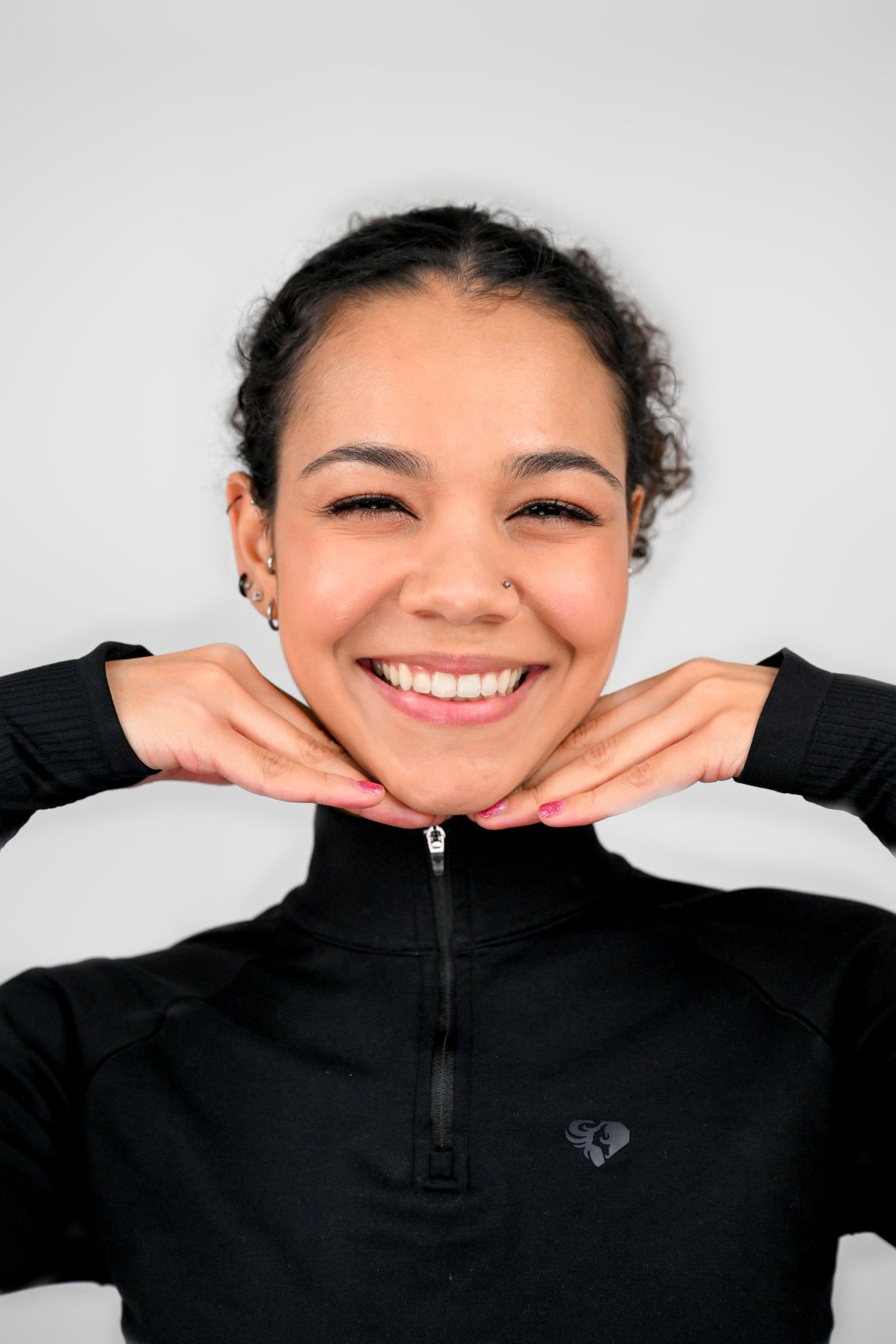 Close-up portrait of someone in black athletic wear with hands under chin.
