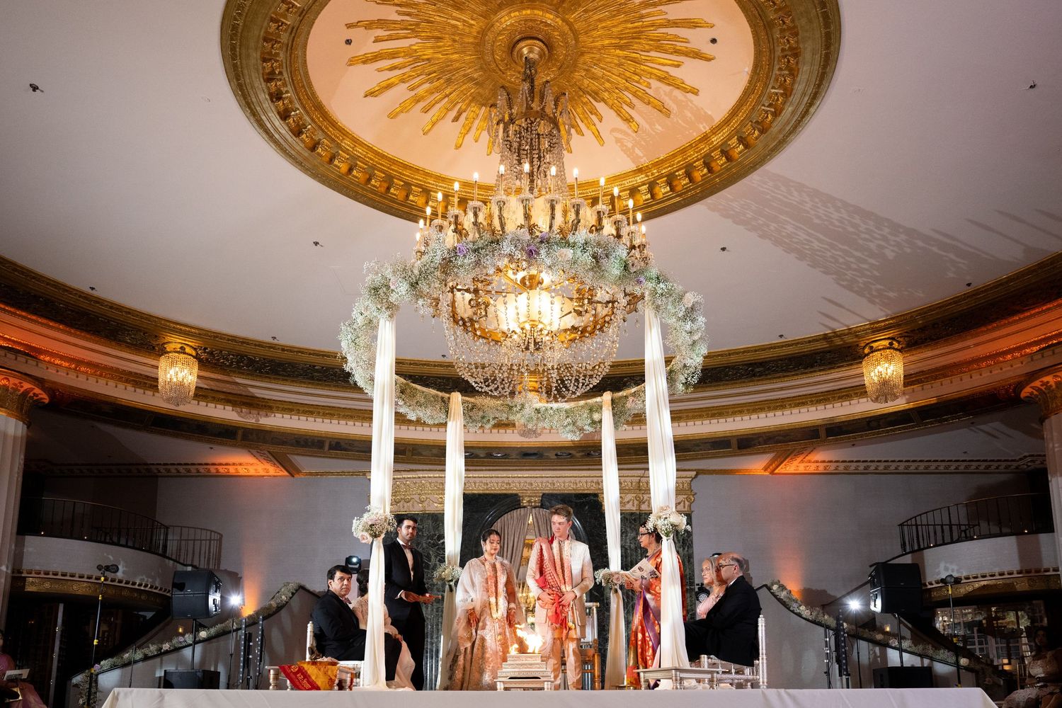 Elegant ballroom with ornate crystal chandeliers and circular ceiling details illuminated in warm lighting.