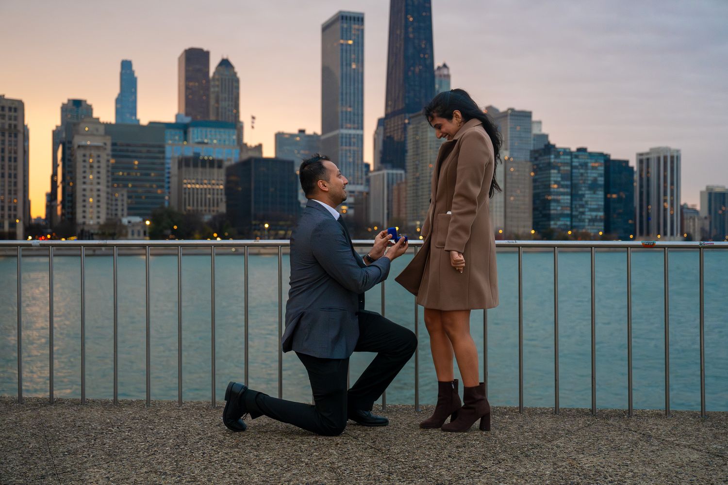 Surprise proposal moment against Chicago skyline during sunset at waterfront.