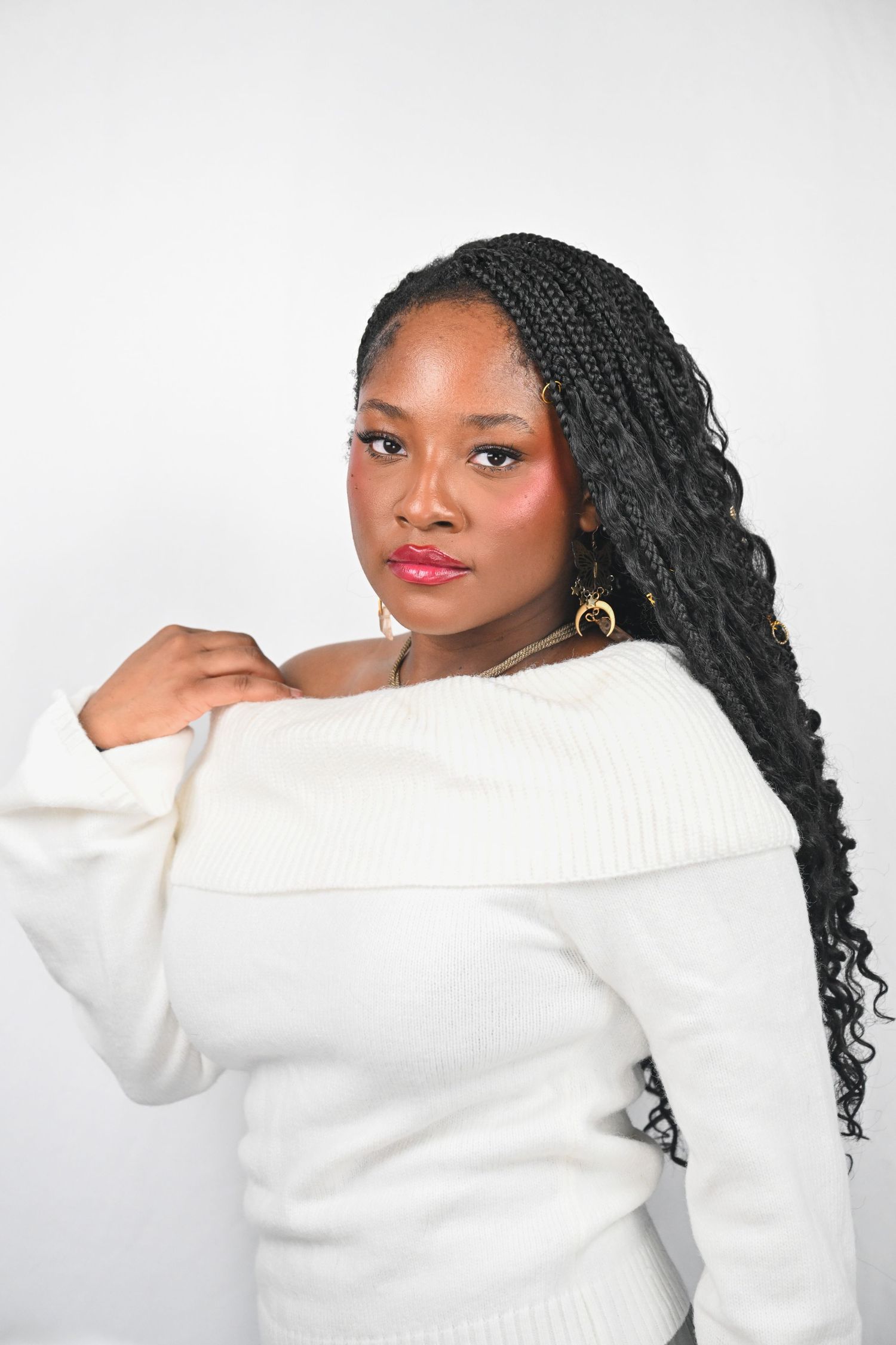 Portrait in white off-shoulder sweater with long braided hair and gold earrings.