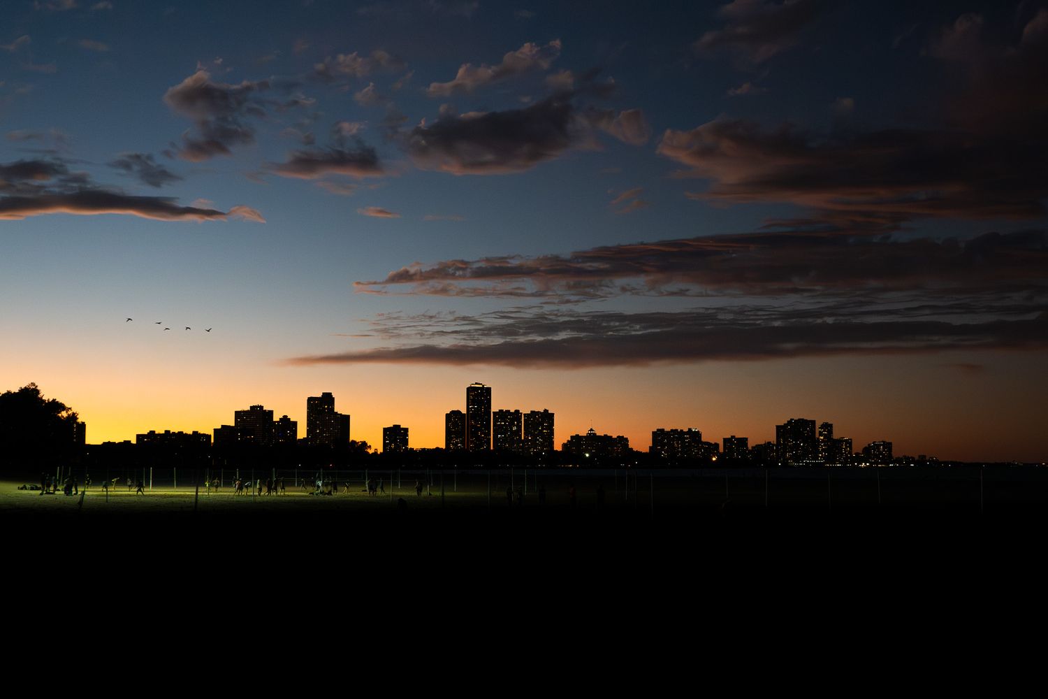 Urban skyline silhouetted against orange and blue sunset sky with dark foreground.