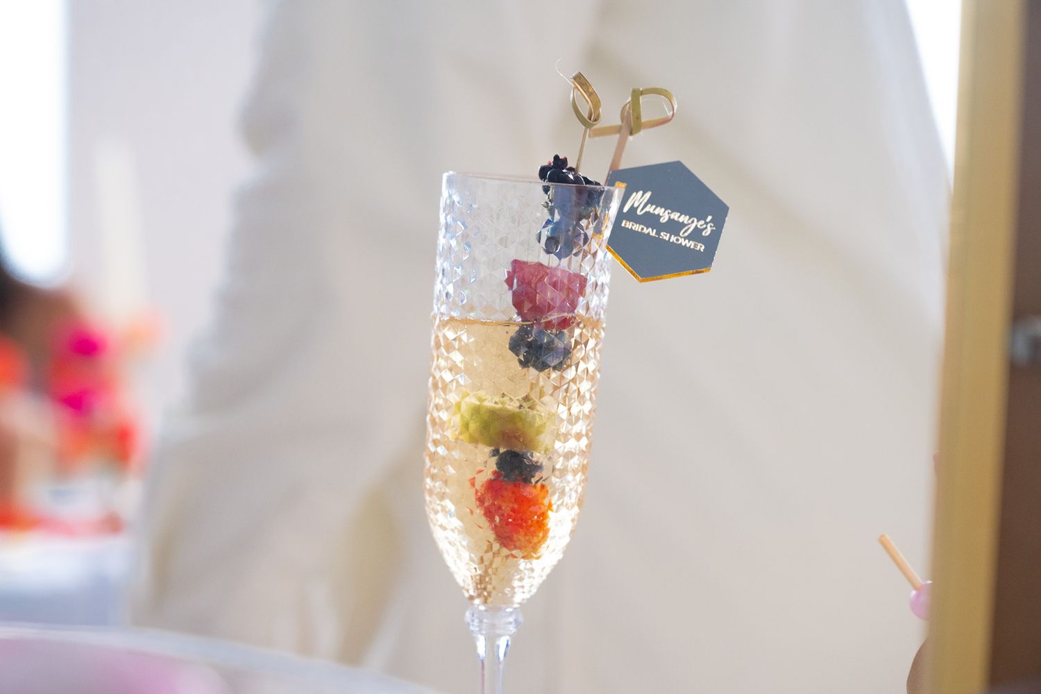 Close-up of a champagne flute with fruit garnish and decorative tag.