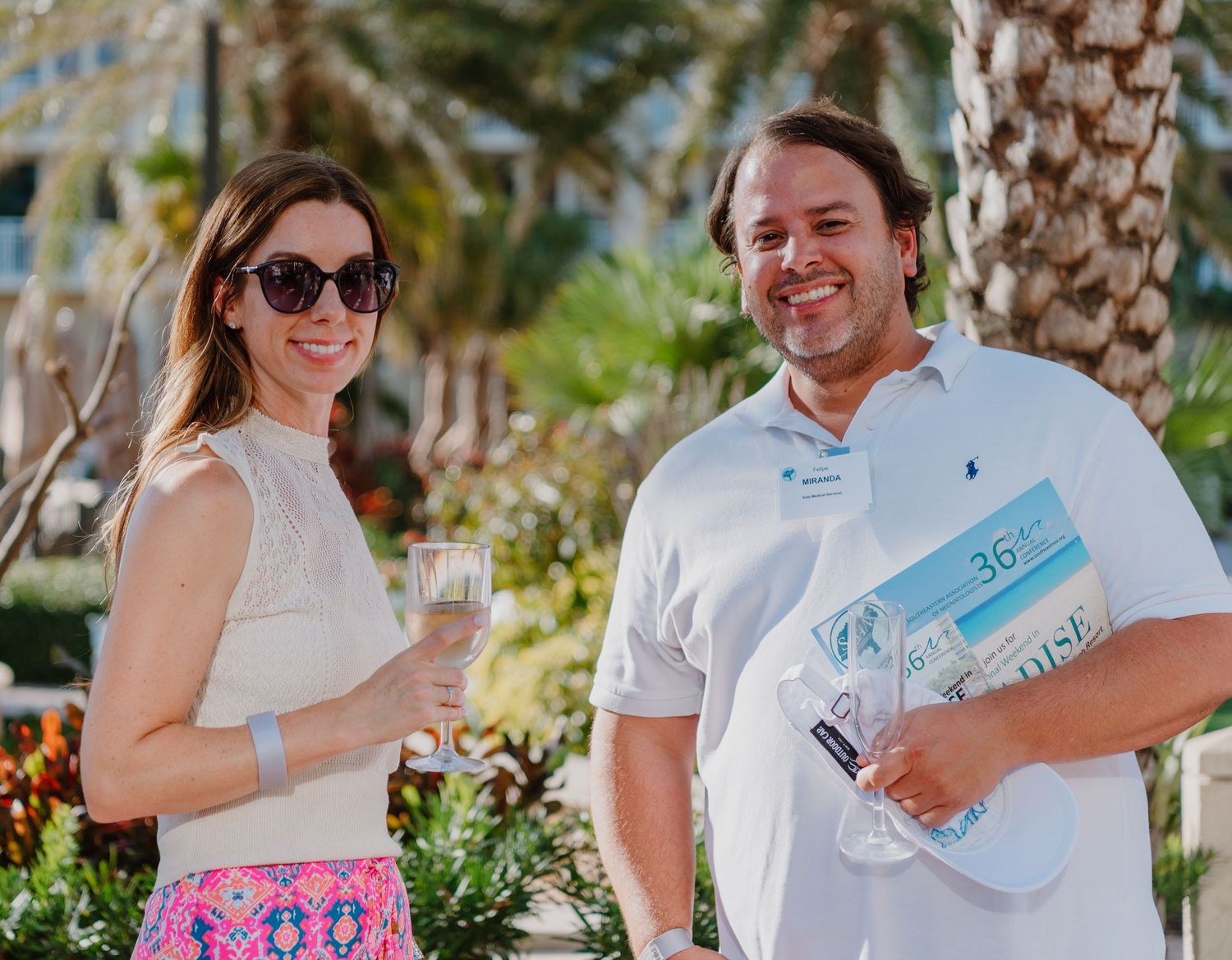 A couple in white clothing walks near palm trees in a tropical resort location.