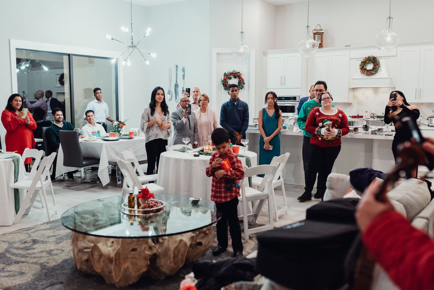 A group of people gathered in a modern living space for a holiday celebration with elegant white furniture and decor.