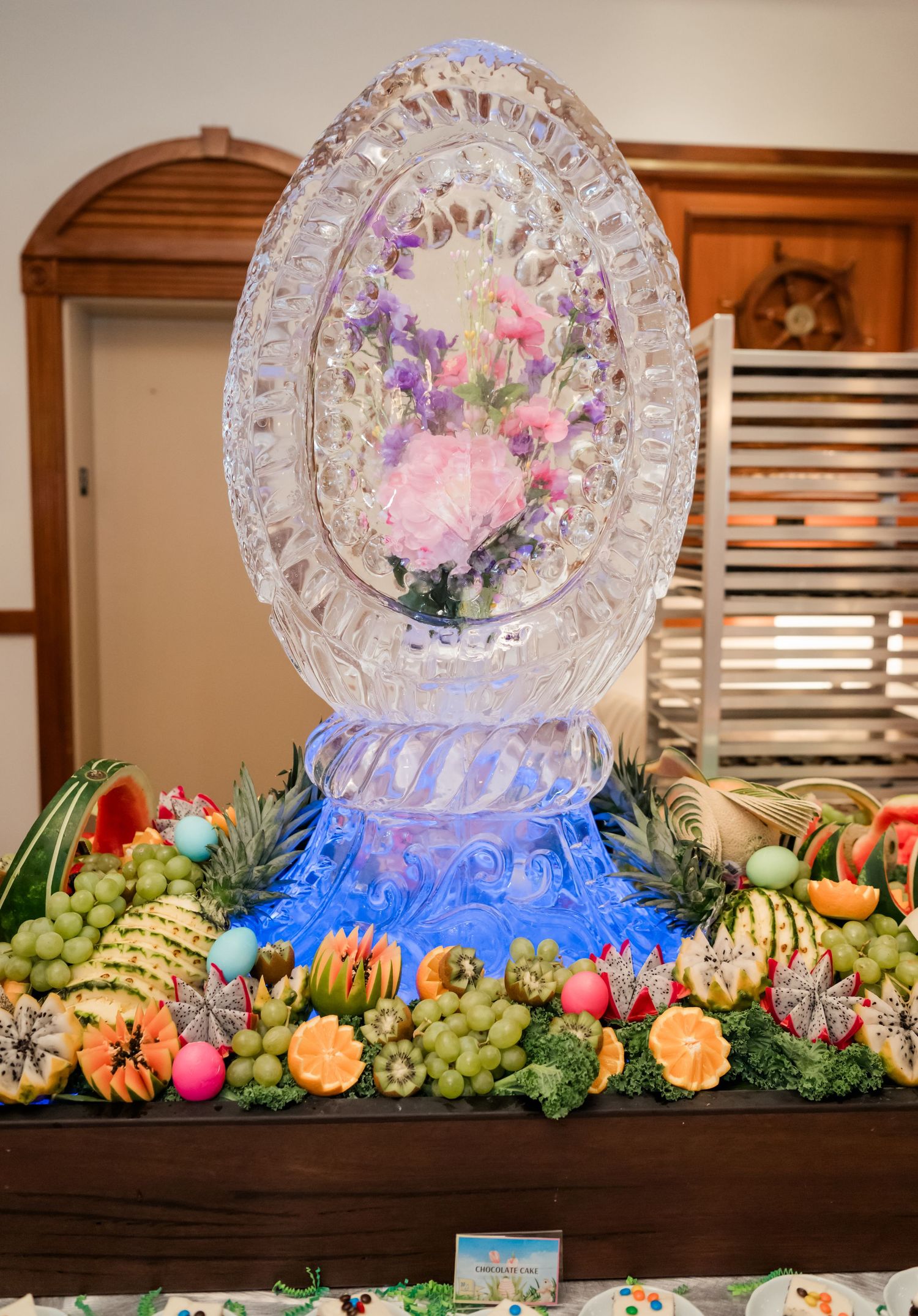 Elegant ice sculpture centerpiece surrounded by colorful fresh fruit display at an event.