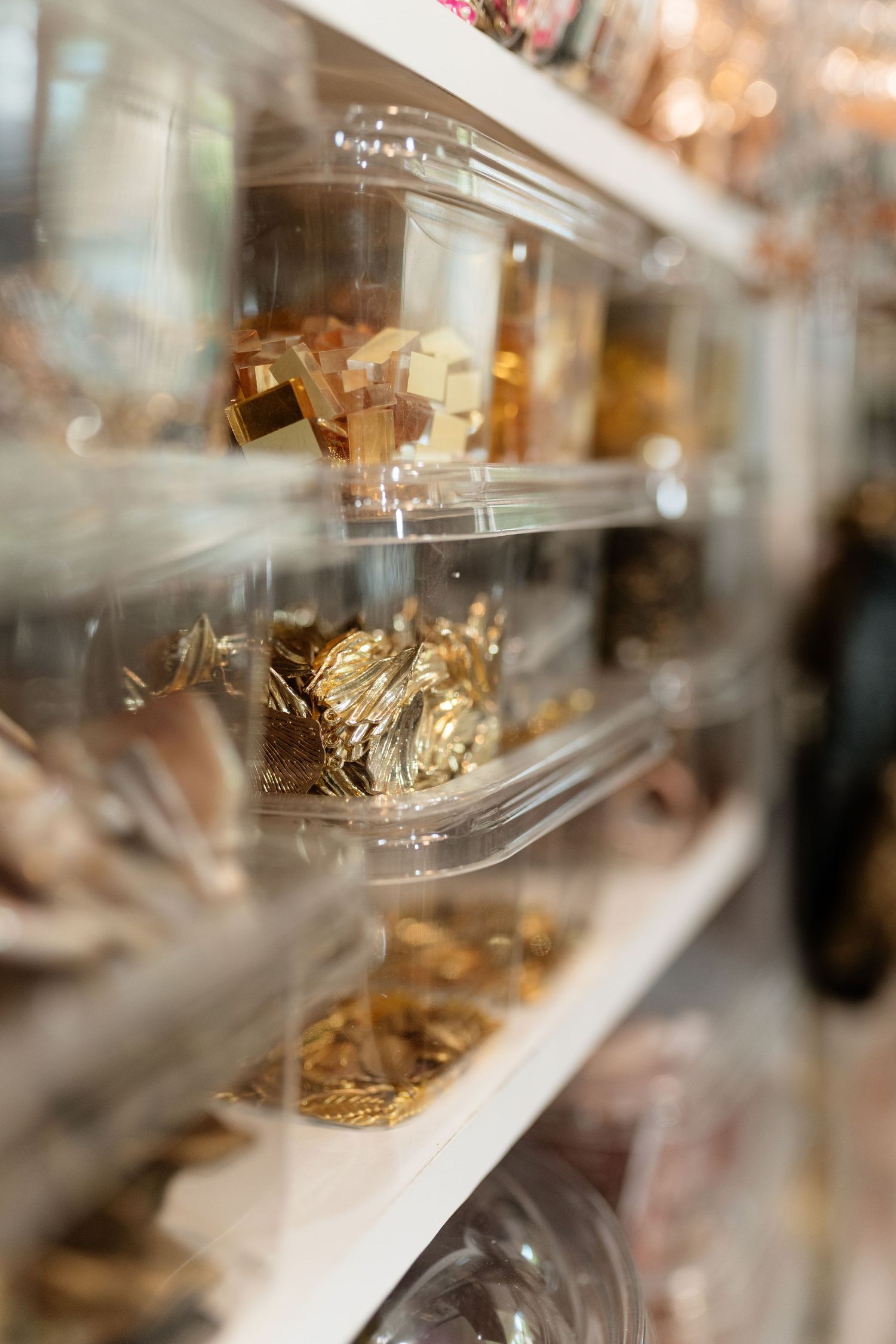 Gold jewelry and accessories displayed on clear acrylic shelves in a boutique or craft studio setting.