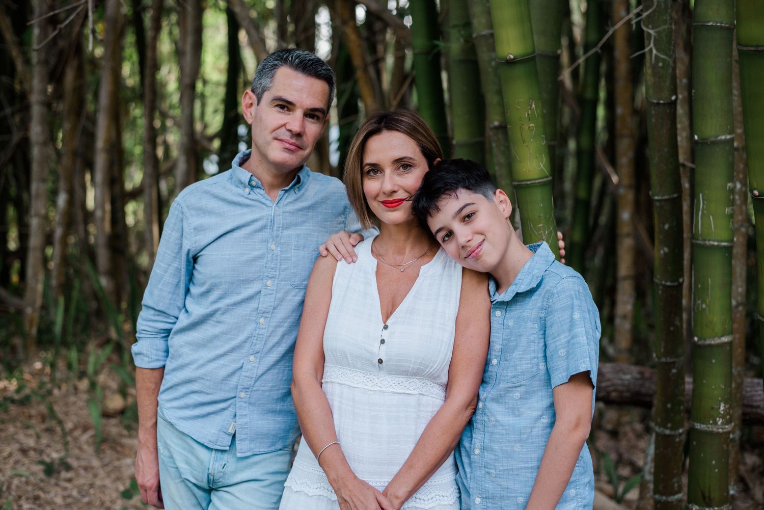 Three people stand together smiling in front of tall green bamboo stalks in a forest setting.