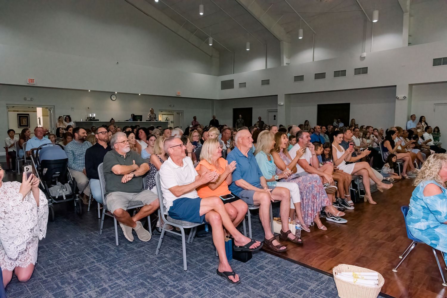 A panoramic view of people sitting in rows of chairs during an indoor event with bright lighting.