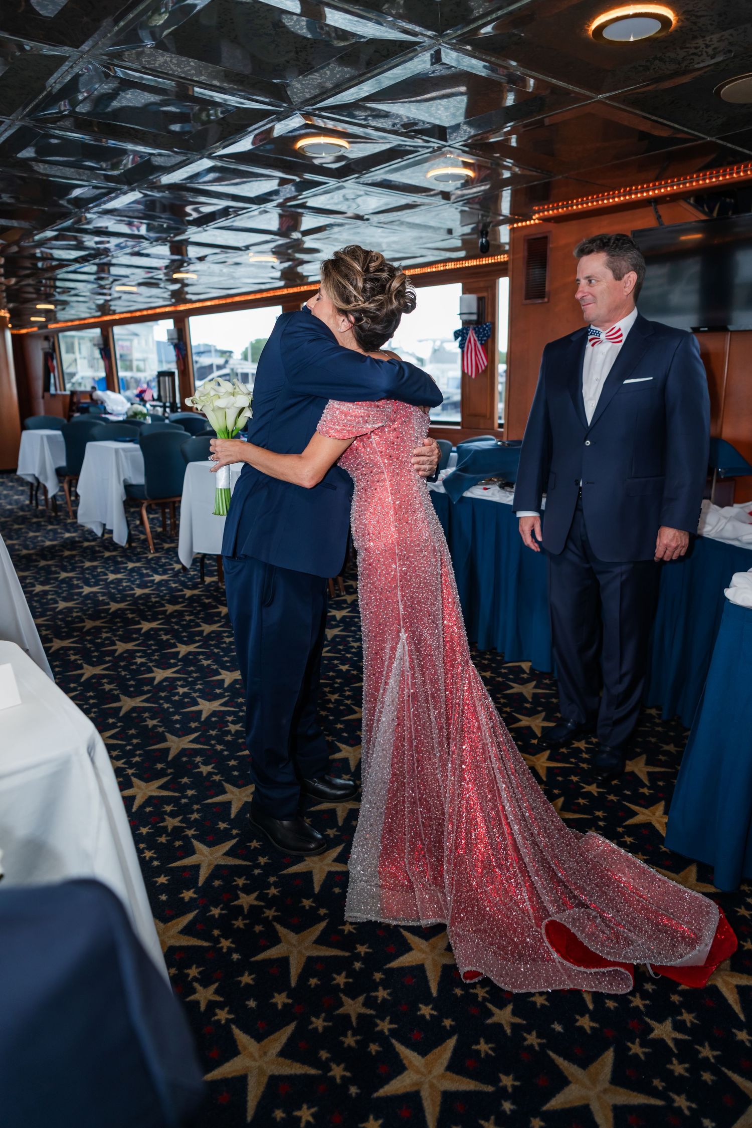Couple embracing in elegant red gown on a cruise ship dining room, man in navy suit watches nearby.