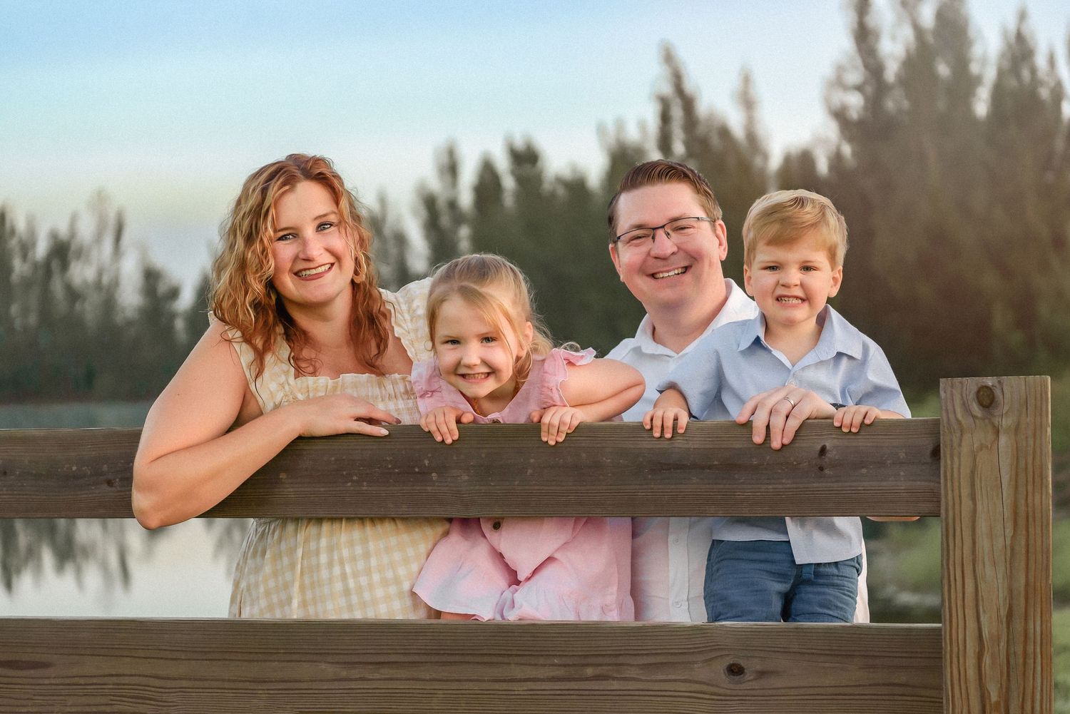 A family poses together on a wooden fence during an outdoor photo session at sunset.
