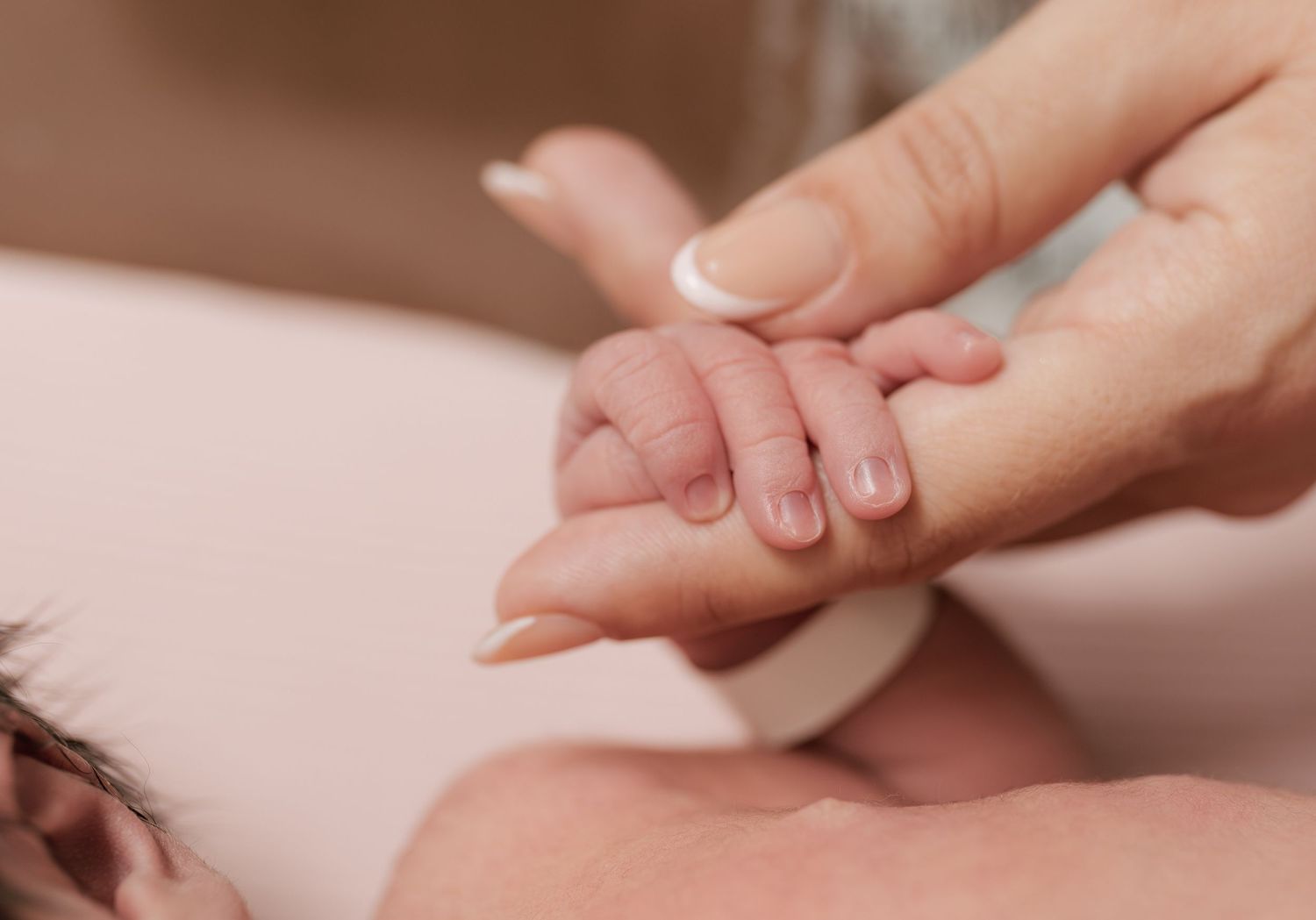 Adult hand gently holding a newborn baby's tiny hand in a tender, loving moment of connection.