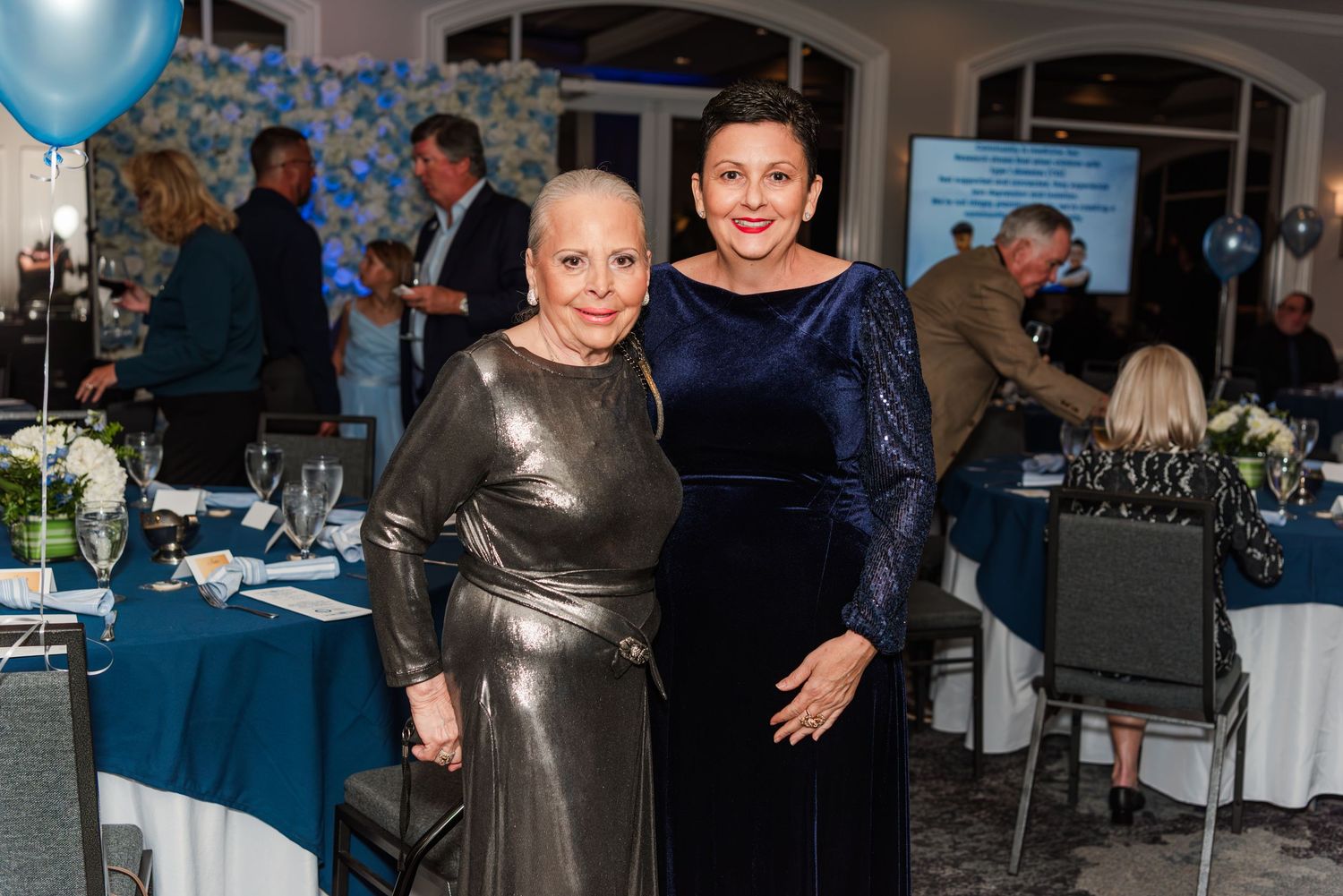 Elegant party guests mingle and socialize at an upscale indoor event with blue lighting and formal attire.
