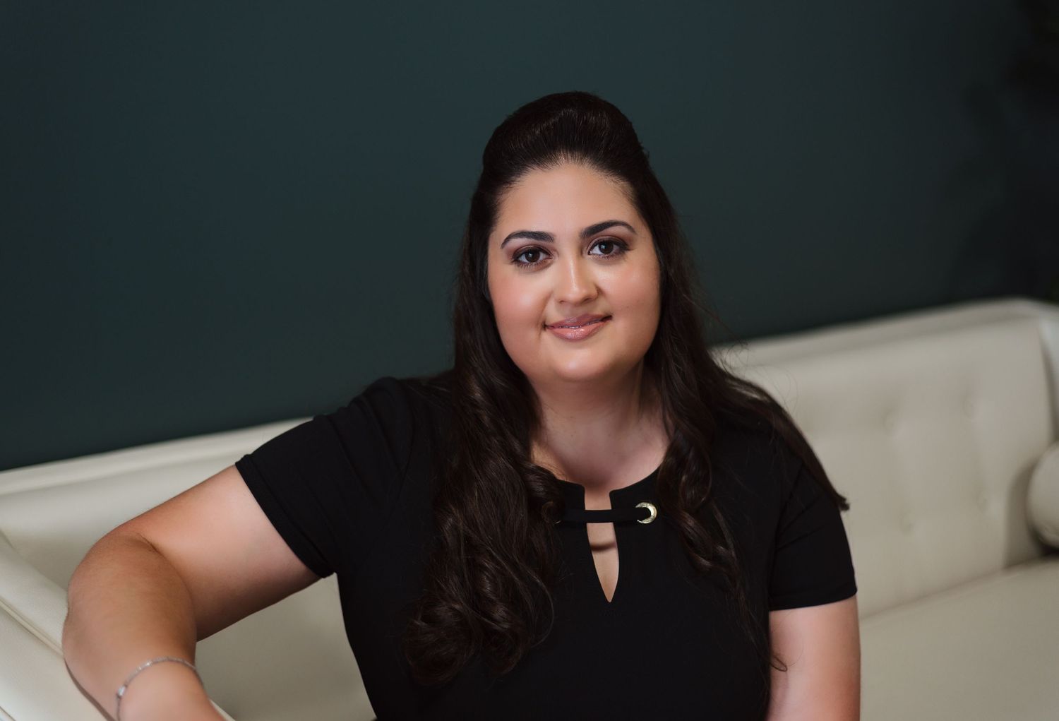 A person wearing a black t-shirt sits comfortably on a light-colored sofa against a dark green wall.