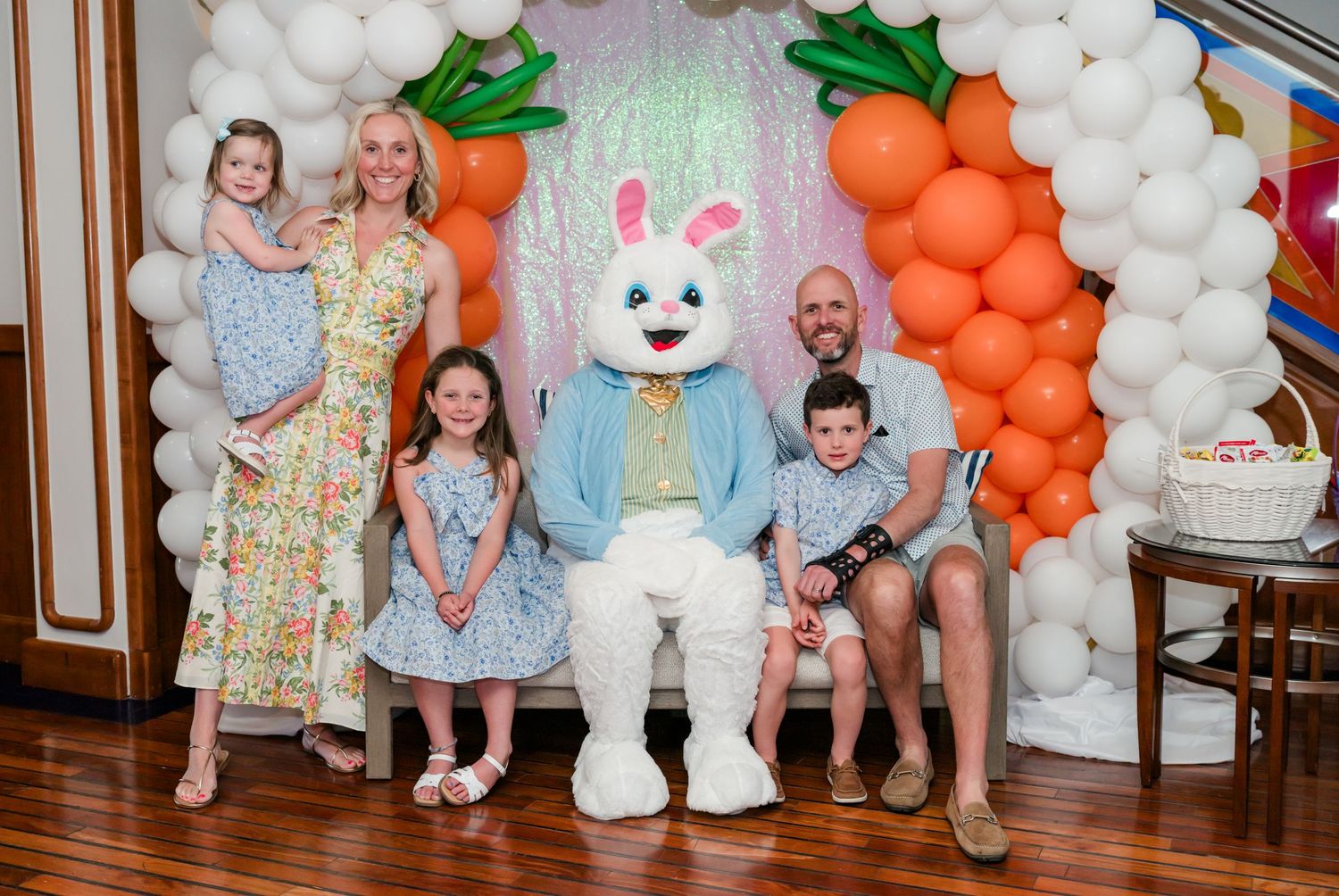 Family posing with Easter Bunny character in front of carrot and balloon arch decoration.