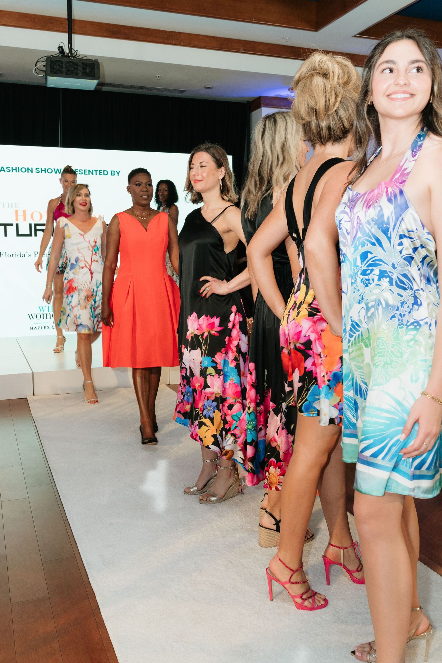 Models walk the runway showcasing colorful summer dresses and resort wear at a fashion show event.