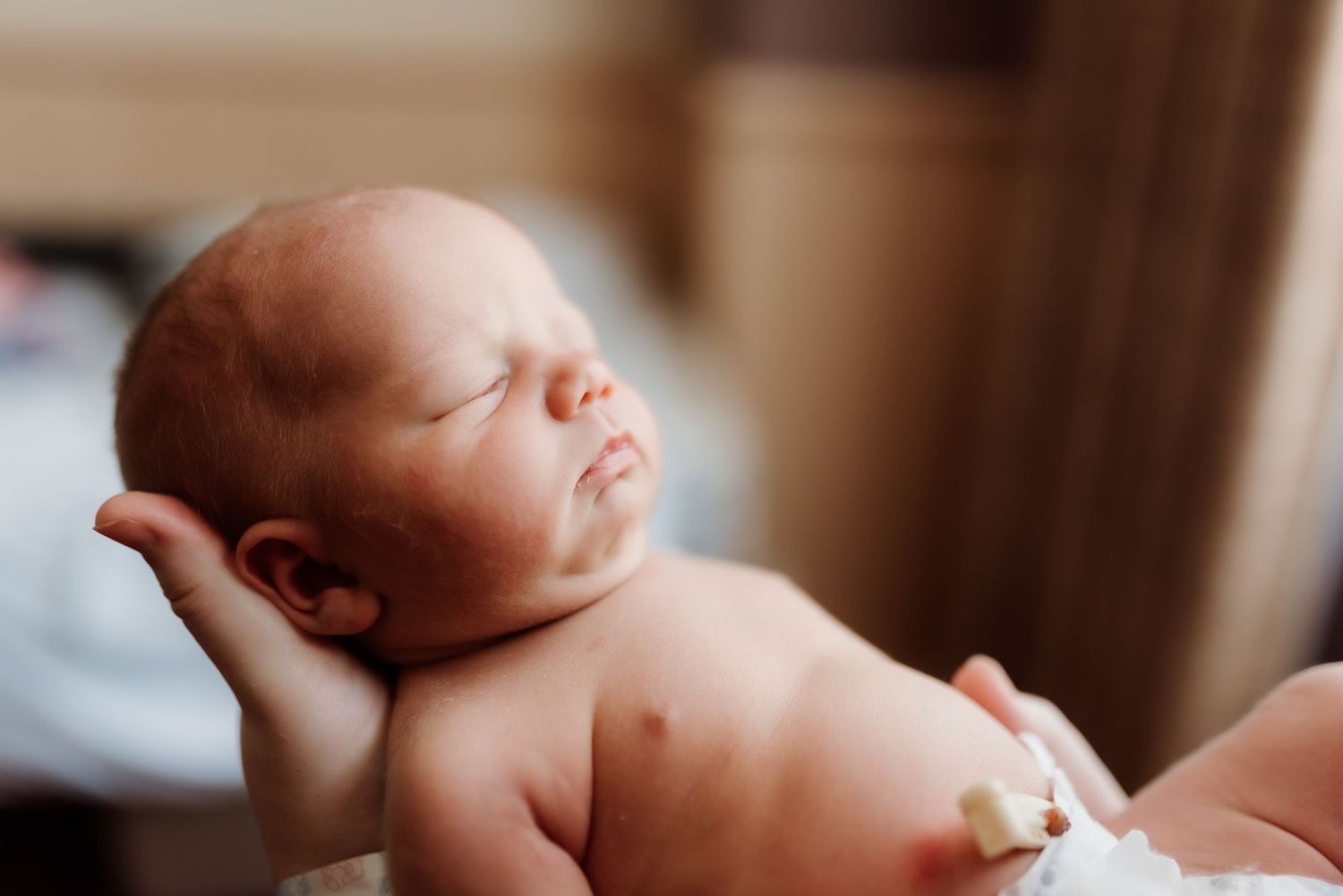 Peaceful newborn baby sleeping soundly on soft beige blanket in natural lighting.