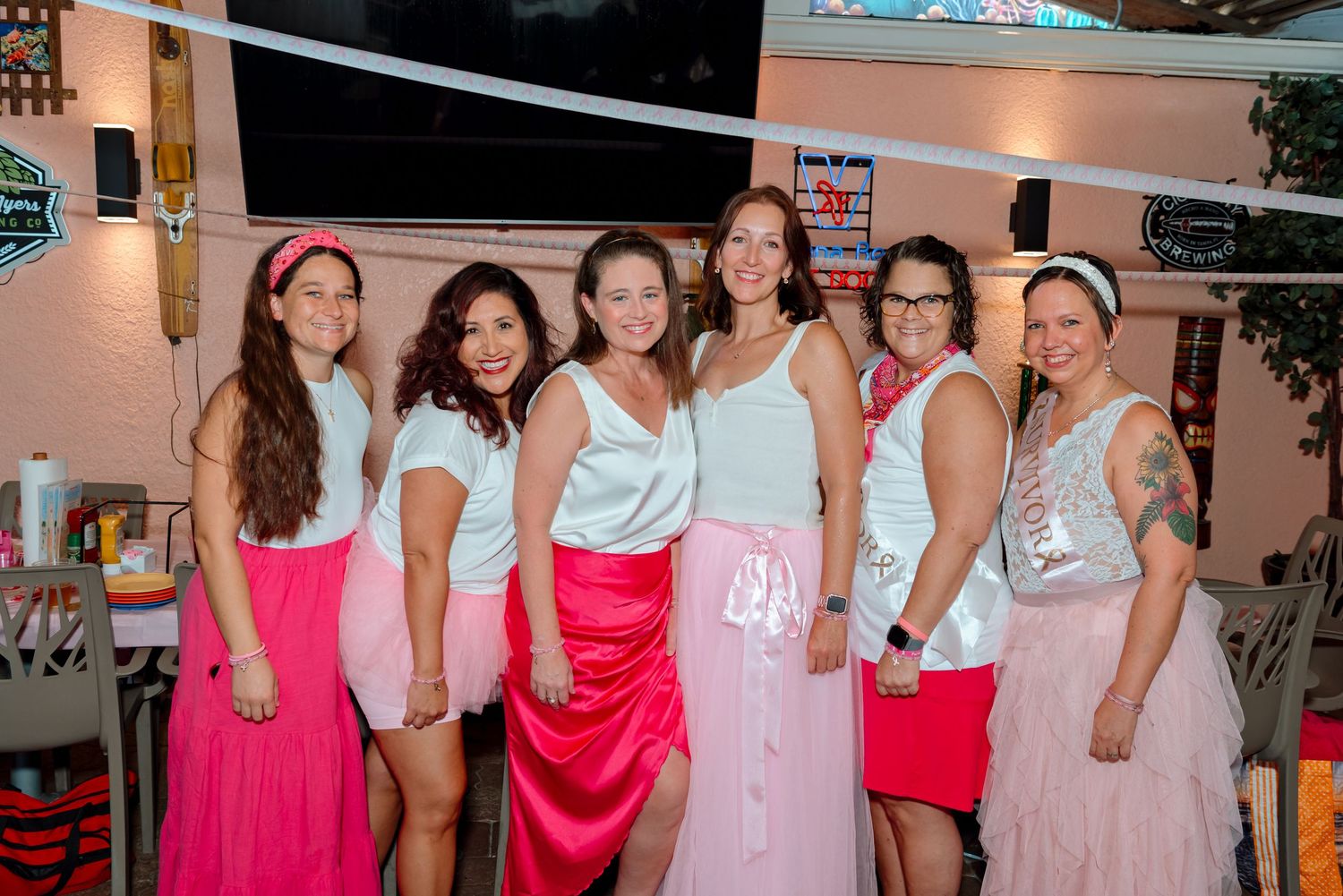 A group in pink and white outfits poses together at a party or social gathering.