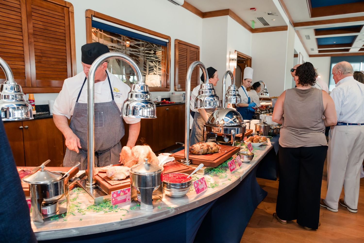 Guests serving themselves at an elegant buffet spread with chafing dishes and fresh food in a upscale restaurant.