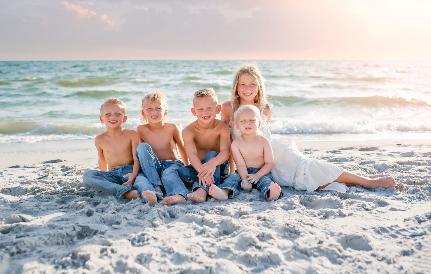 A family lying together on a white sandy beach at sunset enjoying quality time by the ocean.