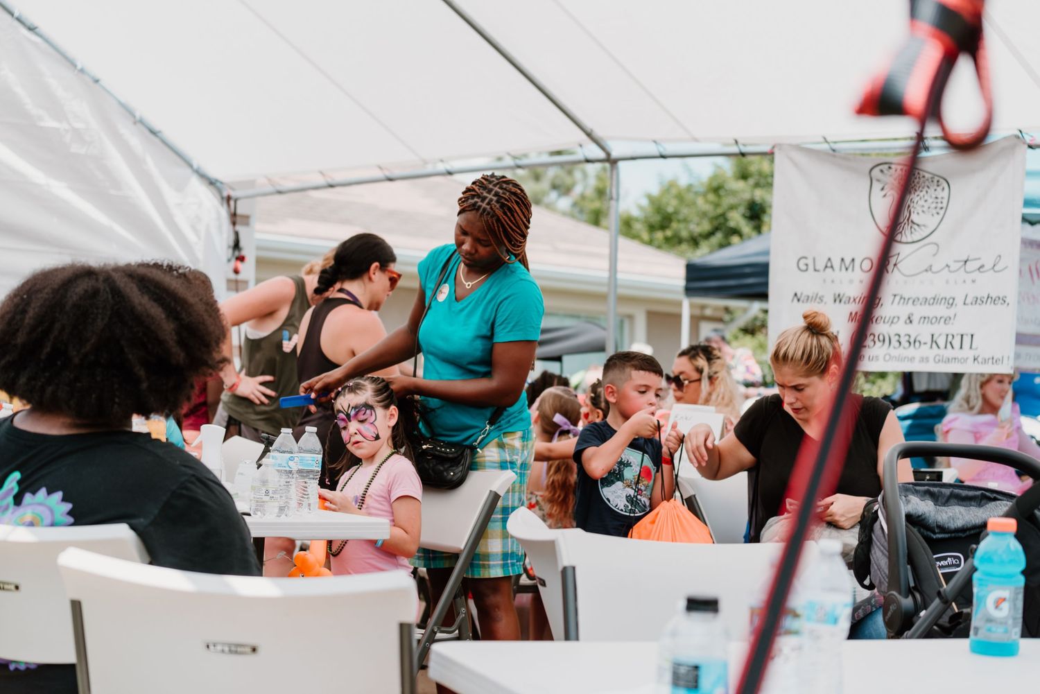 People gather under a white tent at an outdoor community event with tables and chairs set up for dining and socializing.