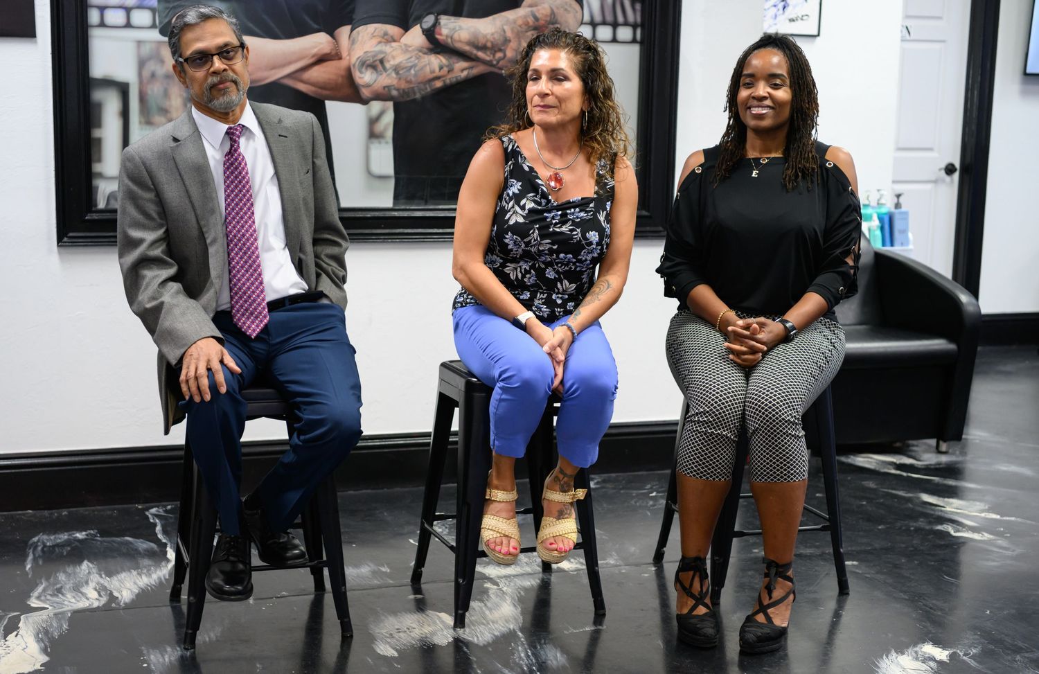 Three people sitting on stools in a tattoo shop, posing for a group photo in a modern studio setting.