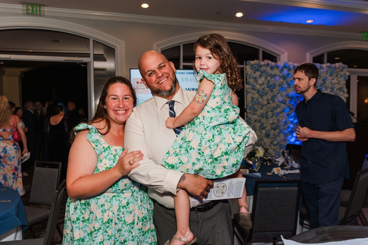 A couple dances together at a wedding reception while wearing a green floral dress and formal attire.