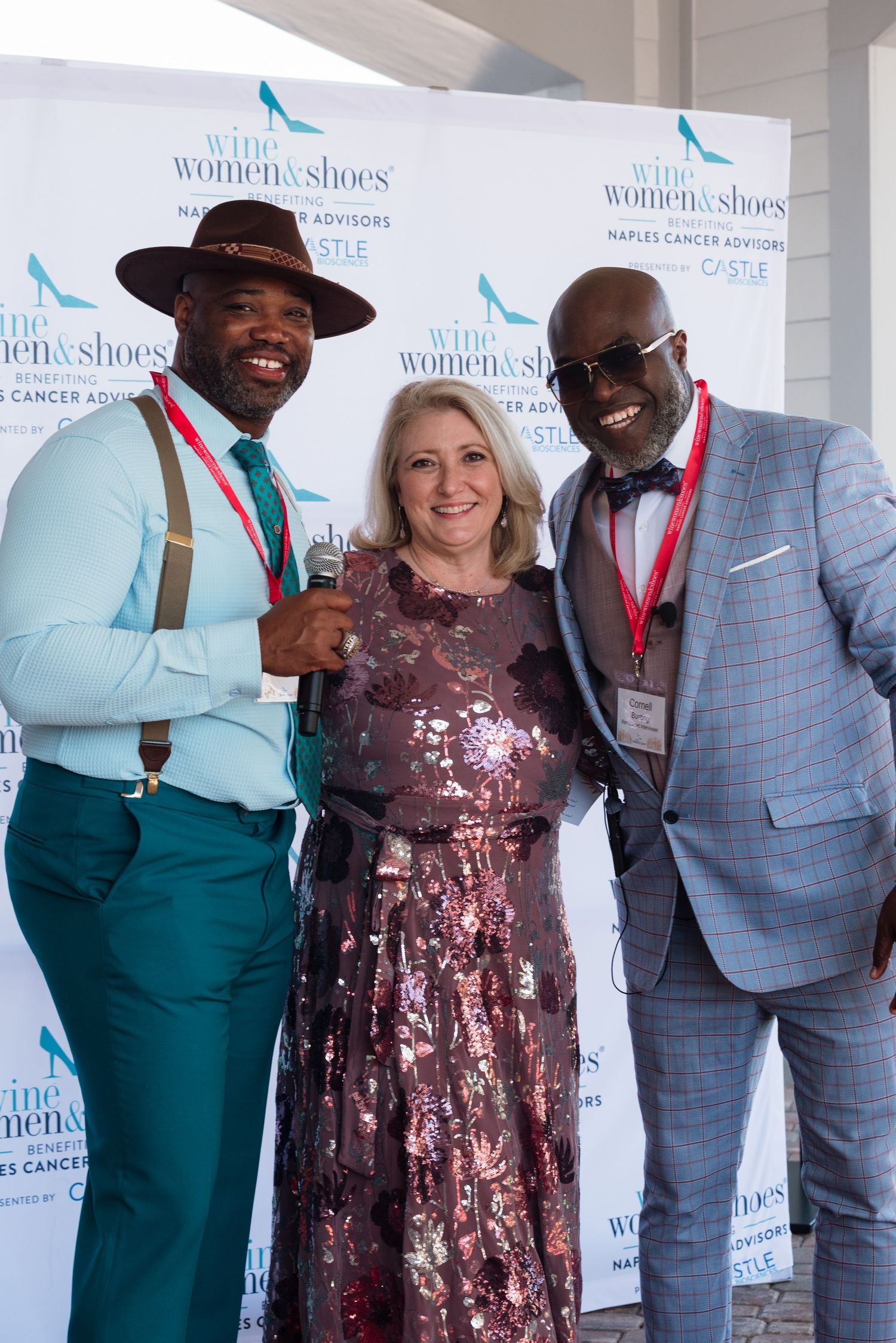 Three stylishly dressed attendees pose at a Women in Shoes charity event backdrop wearing formal attire.