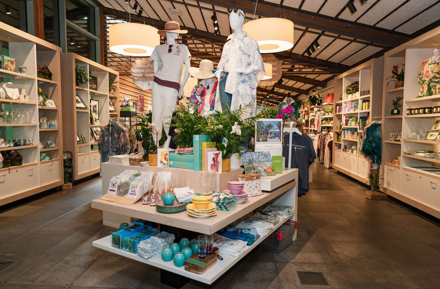 Bright boutique retail store interior with white shelving, clothing displays, and a central table featuring colorful gifts and decor.