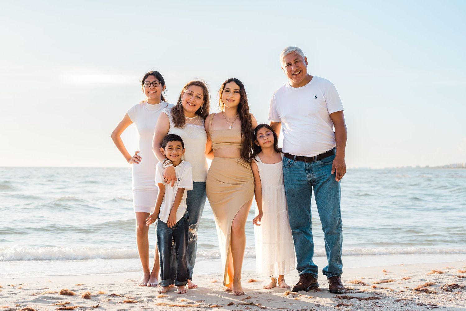 A family group poses together on a sunny beach at sunset with the ocean in the background.