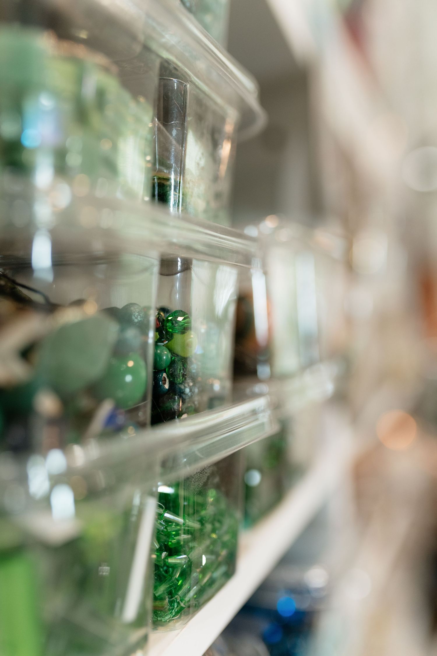 Clear plastic containers filled with green gemstone beads organized on white shelves in a craft store.